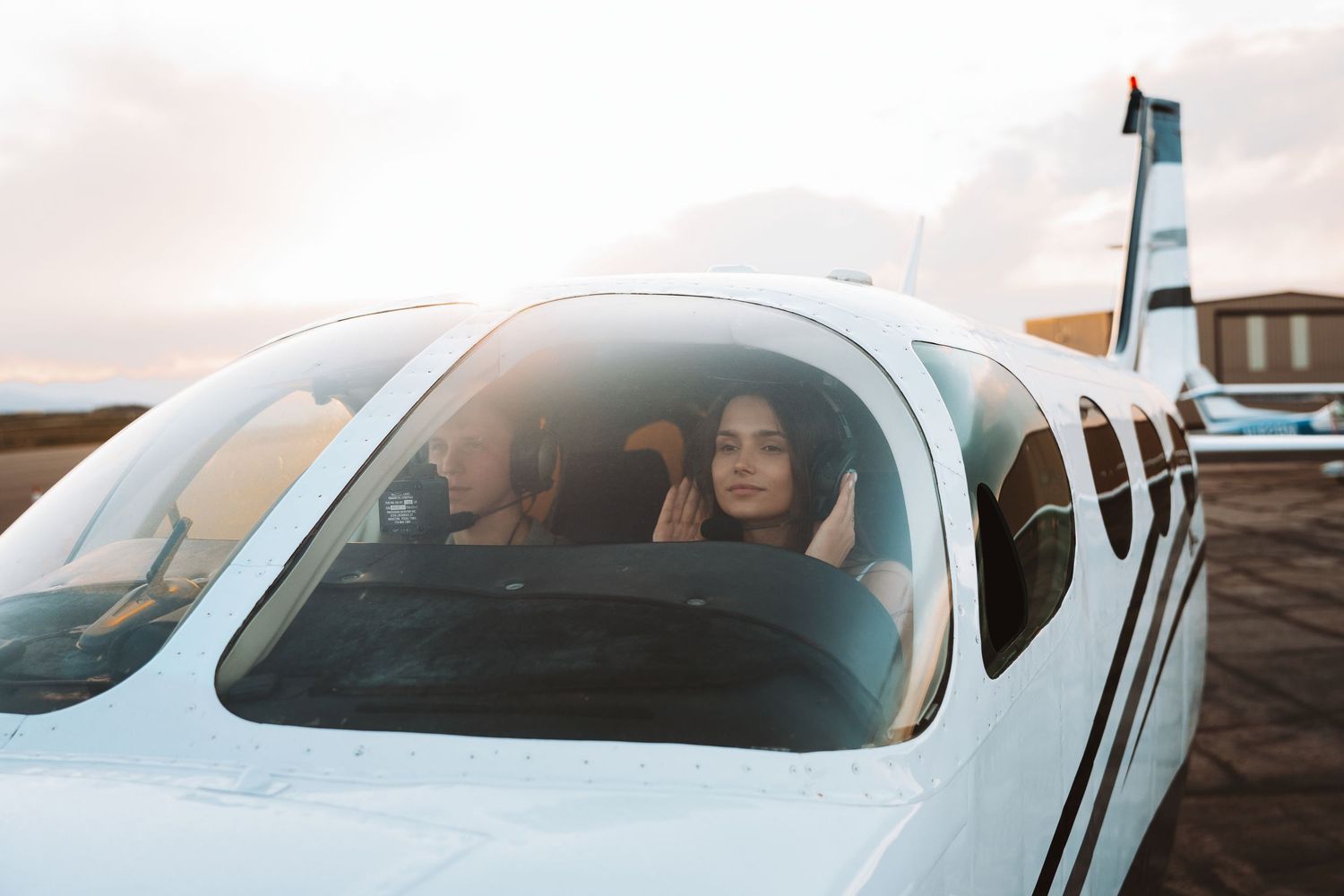 Small private airplane with passengers visible through cockpit window parked on tarmac during golden hour.