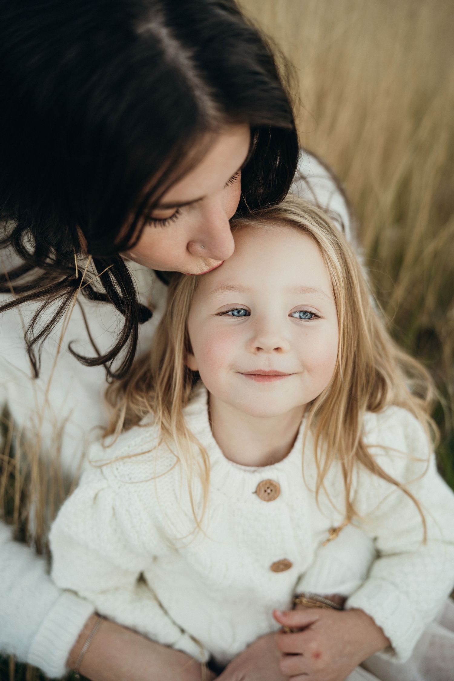 A tender moment captured in warm sunlight shows affectionate interaction between parent and child wearing cream sweaters.