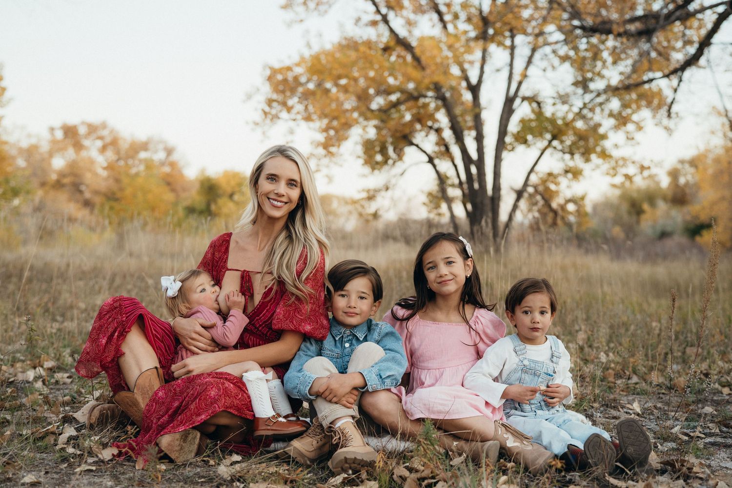 A family group sits together on autumn grass surrounded by golden fall foliage during an outdoor photo session.