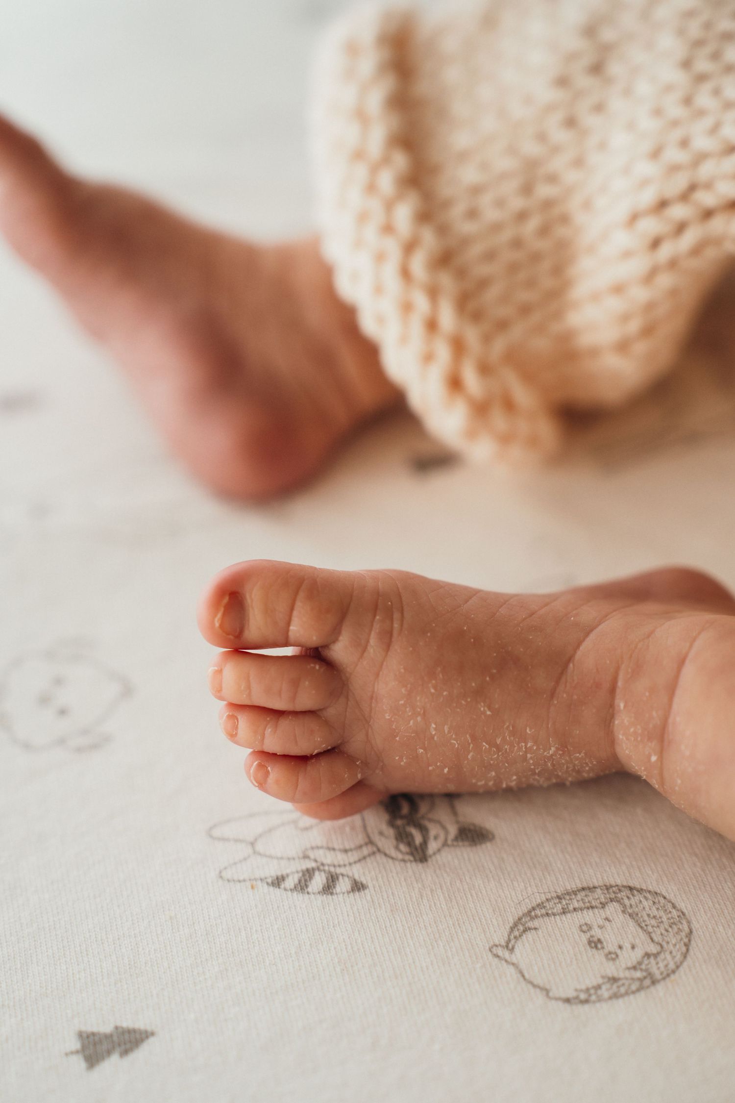 Close-up of tiny baby feet against white fabric with delicate doodle drawings underneath.