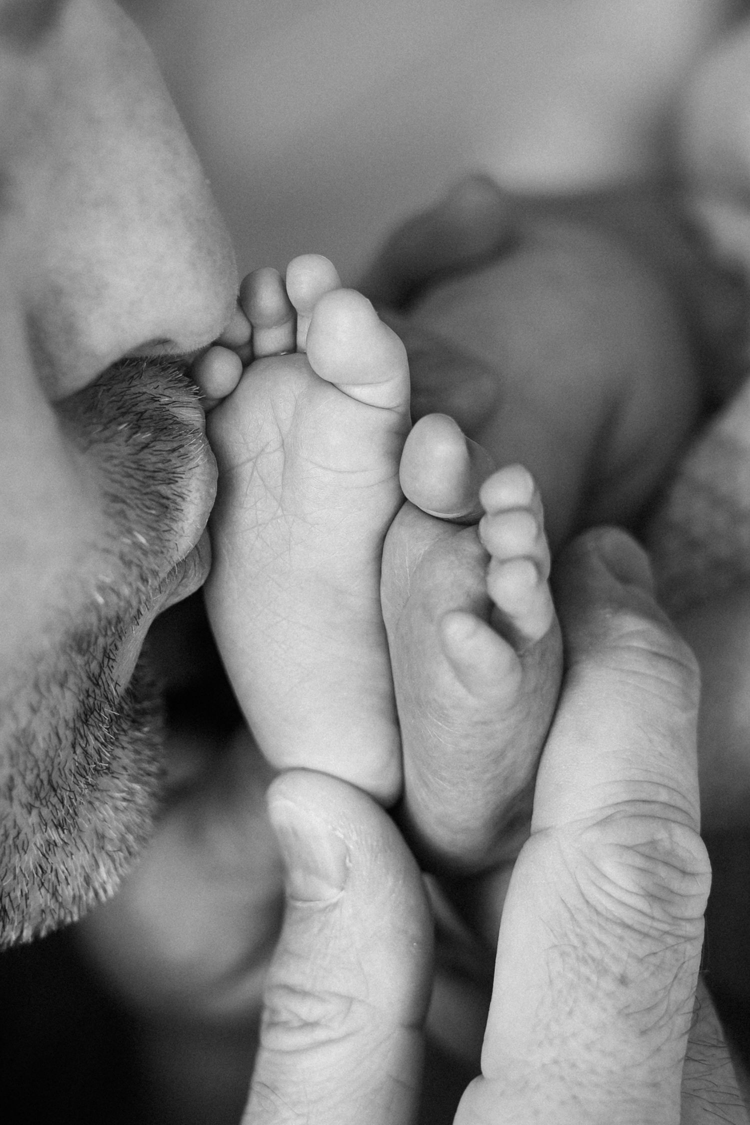 A tender black and white series showing an adult kissing tiny newborn baby toes in close up macro shots.