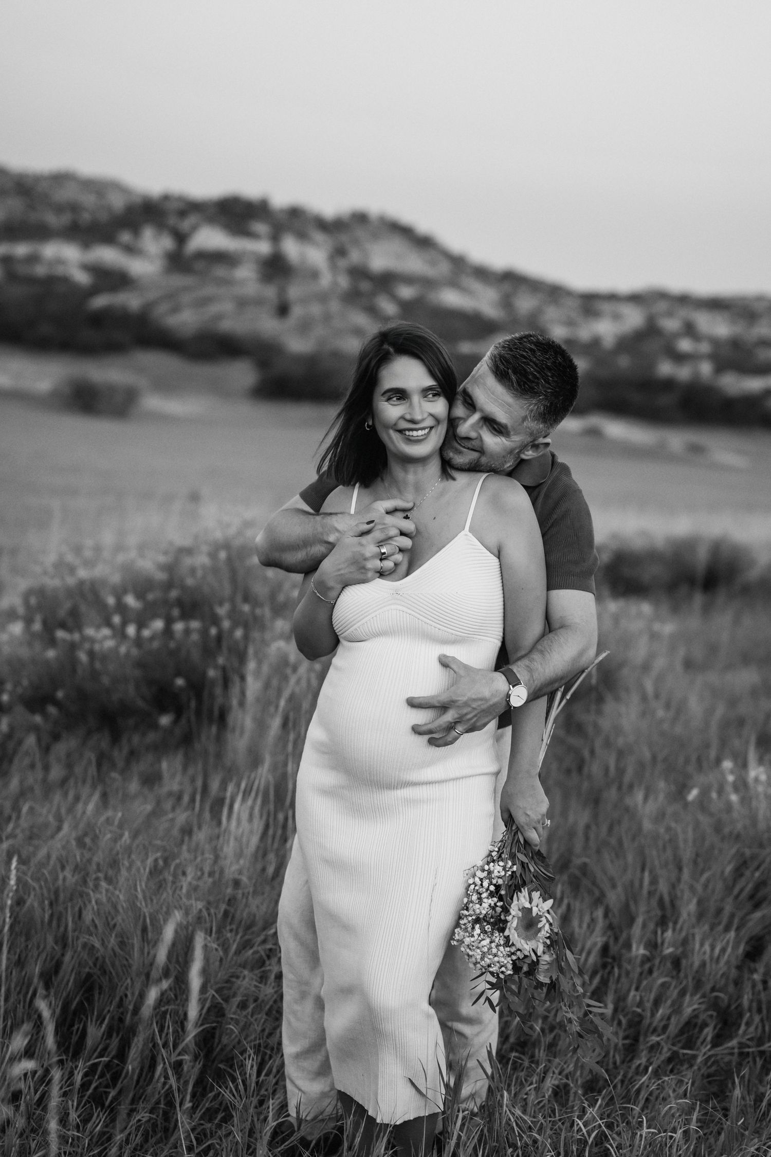 A couple shares an intimate moment in a grassy field during a black and white outdoor photoshoot.
