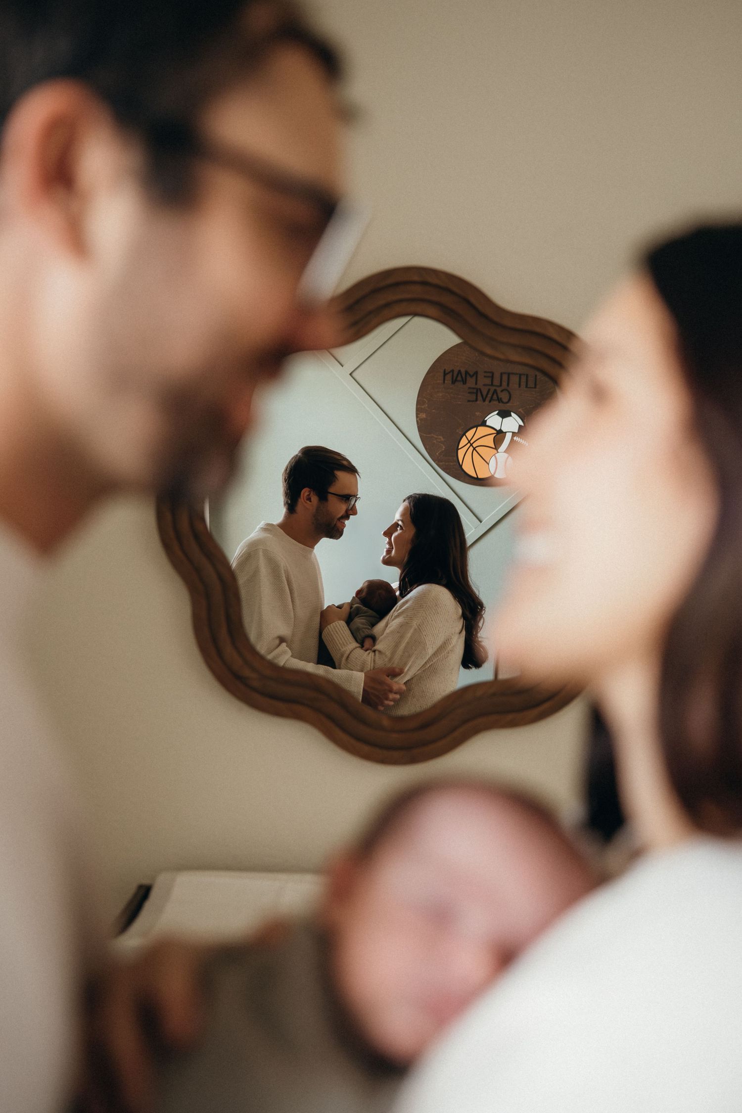 A couple's reflection appears in a wavy-shaped mirror while they share an intimate moment in a softly lit room.