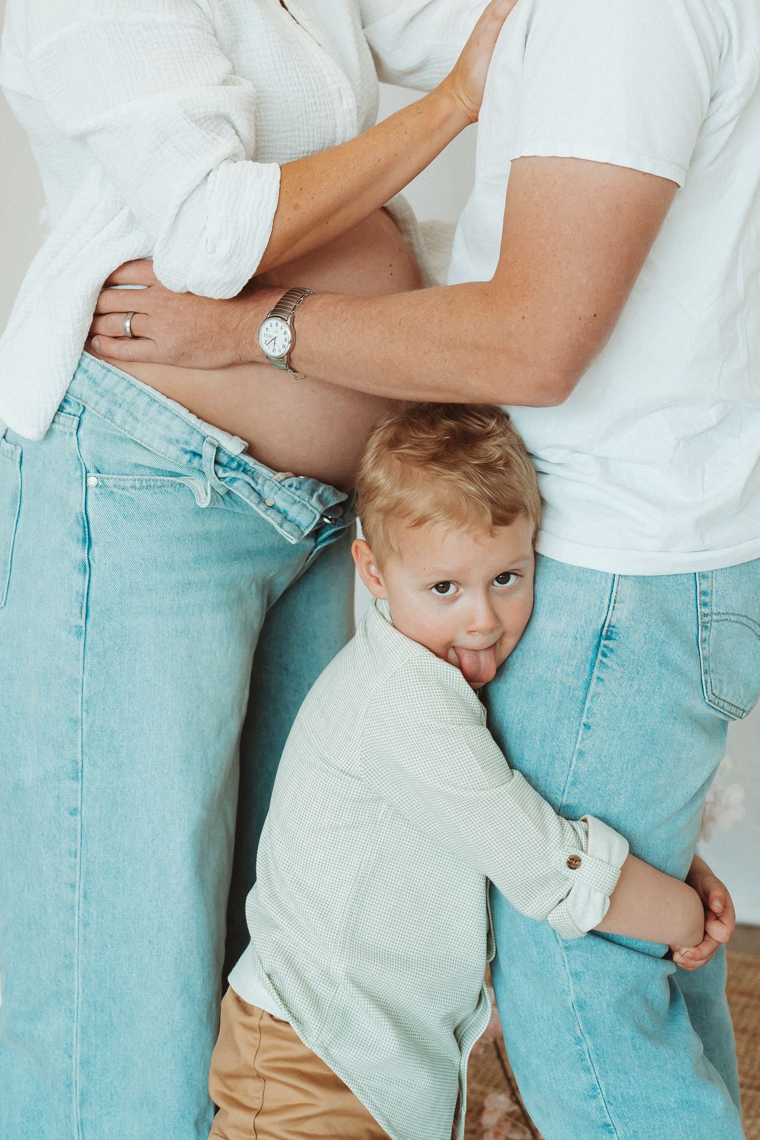 A candid family photo showing a young child hugging their parents while all wearing casual denim and white outfits.