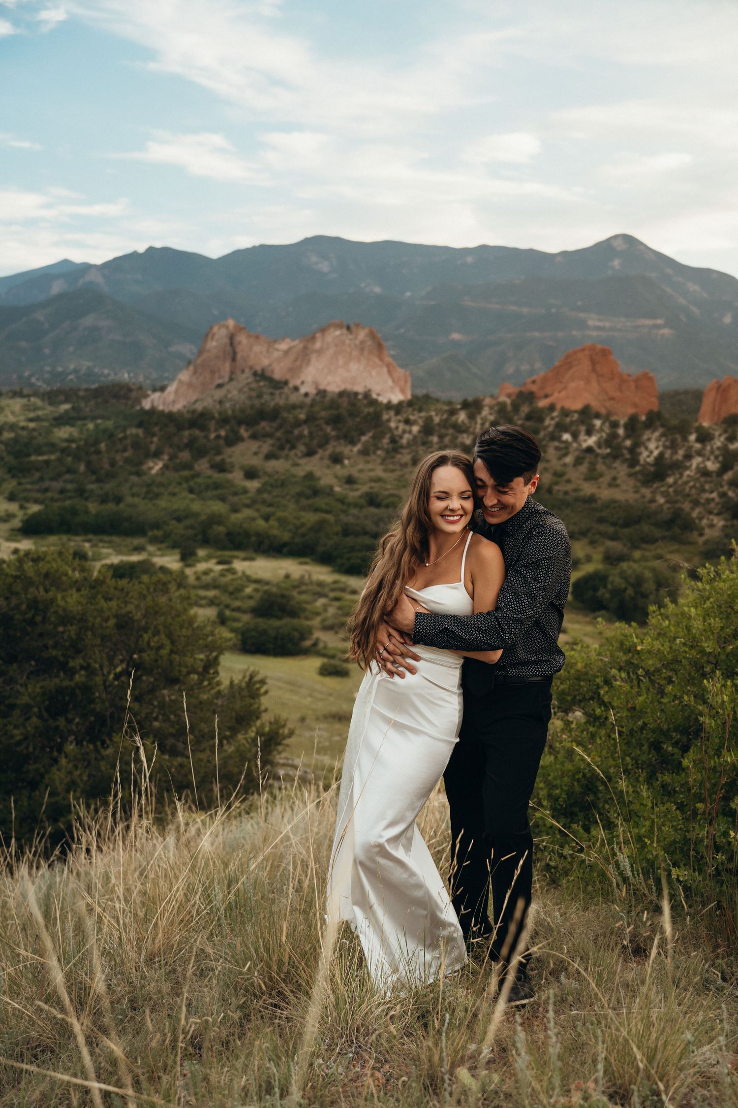 A couple embraces against the backdrop of Garden of the Gods rock formations and mountains in Colorado Springs.