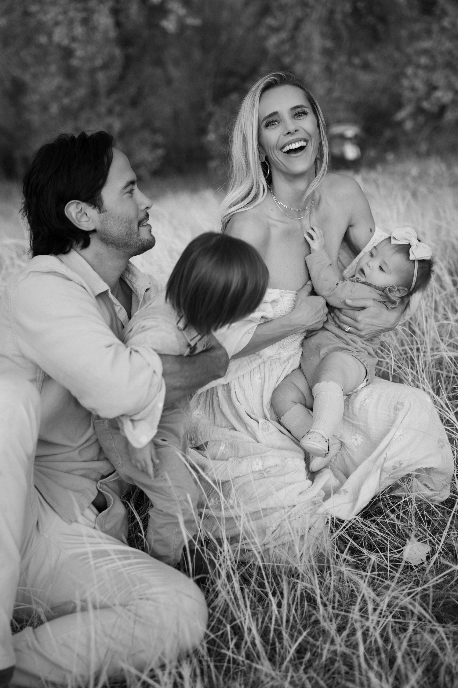 Black and white family portrait captured in tall grass during golden hour.