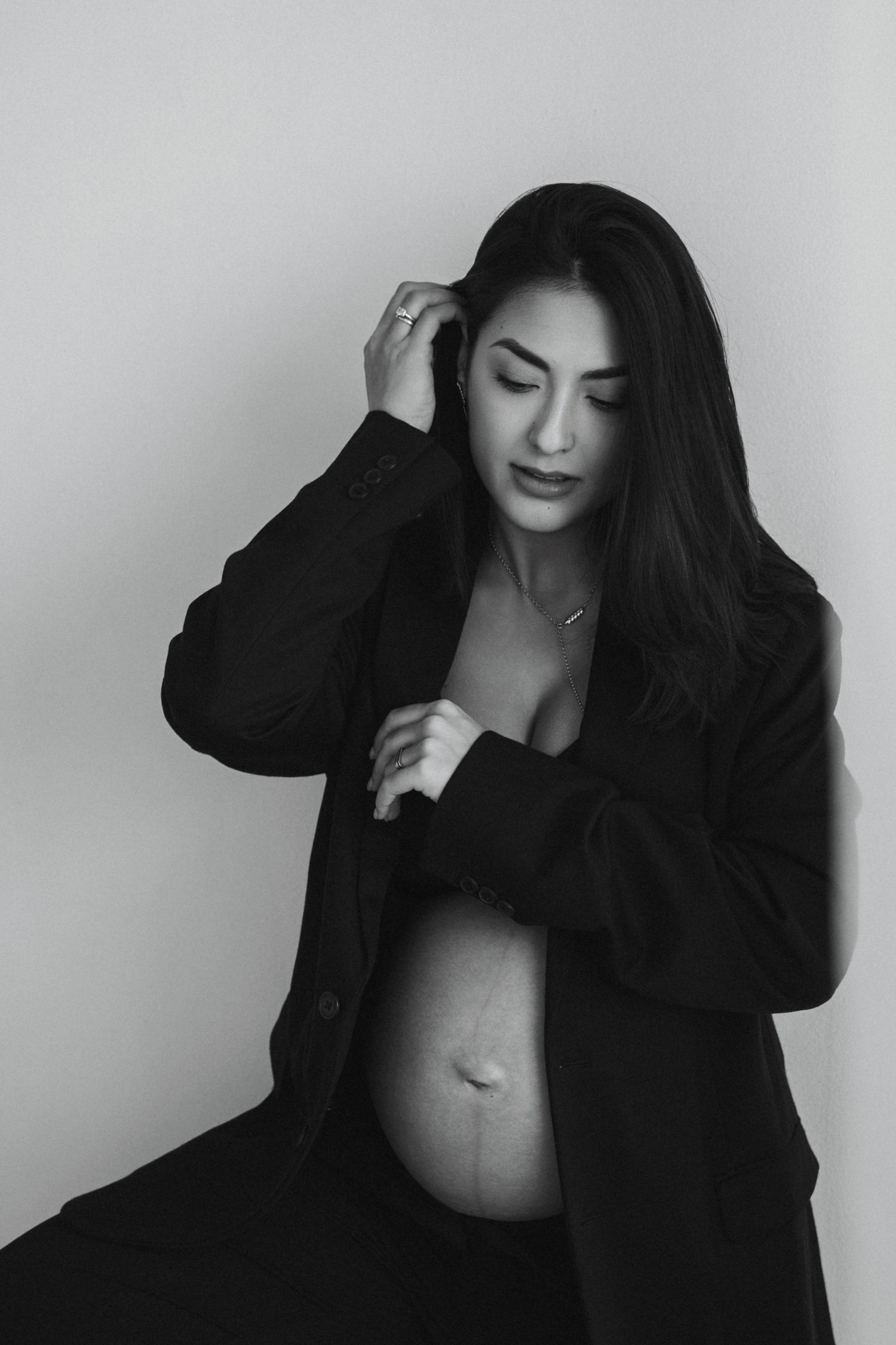 Black and white artistic maternity photo showing woman in black jacket with hand in hair.