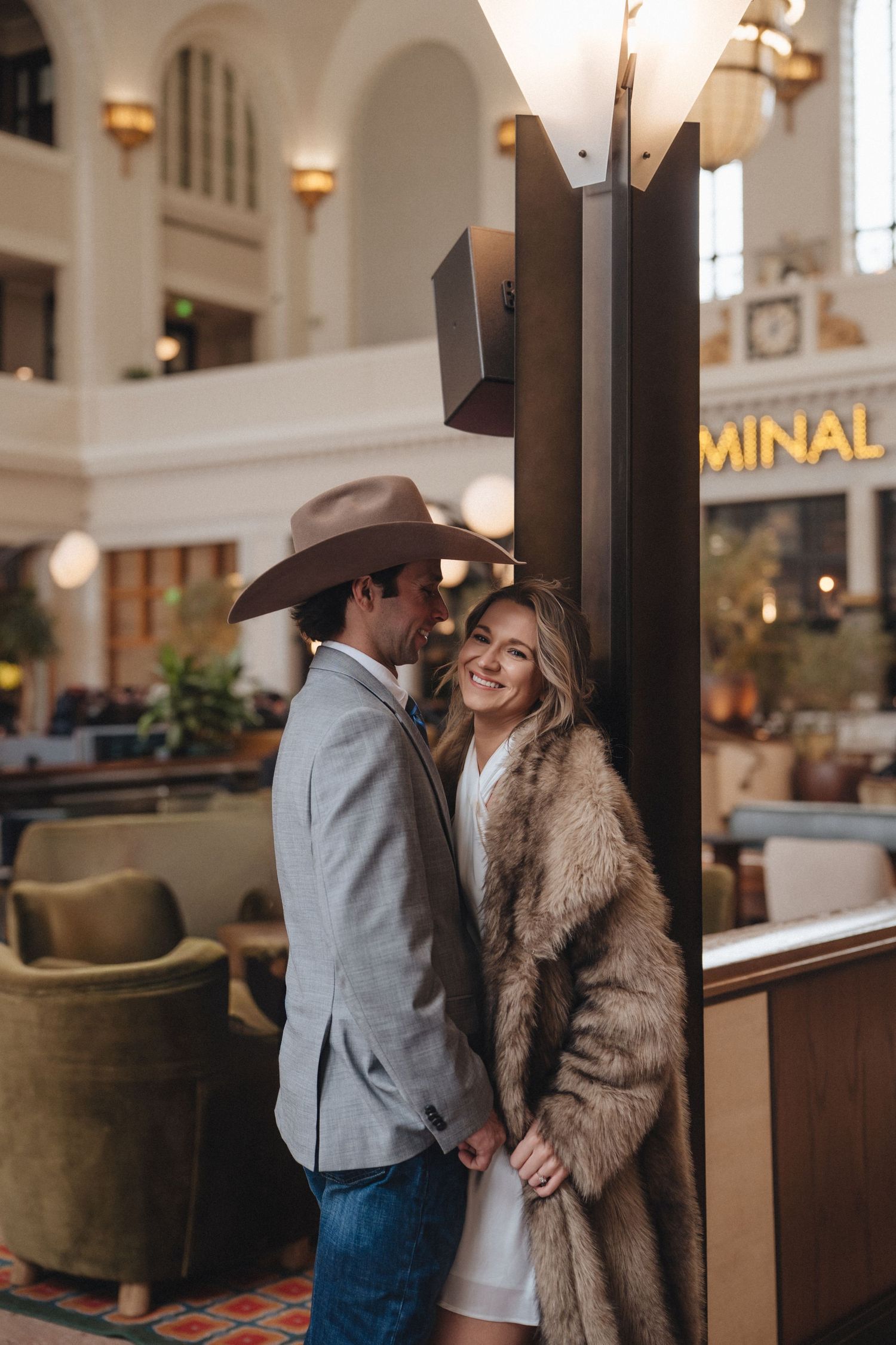 Couple in western attire share romantic moments in an elegant hotel lobby with warm lighting and vintage decor.