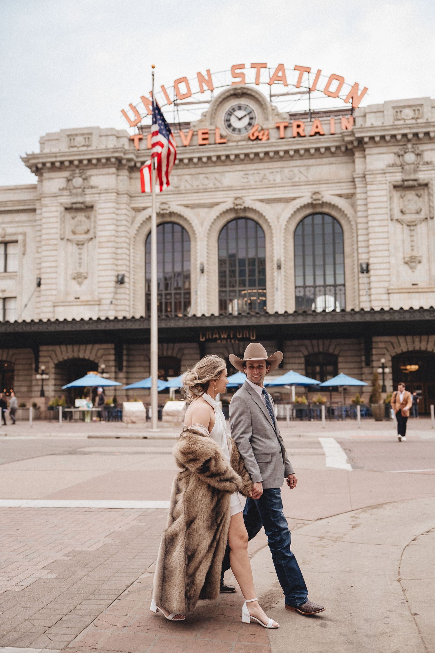 Couple poses together in front of historic Denver Union Station building in a romantic engagement photo series.