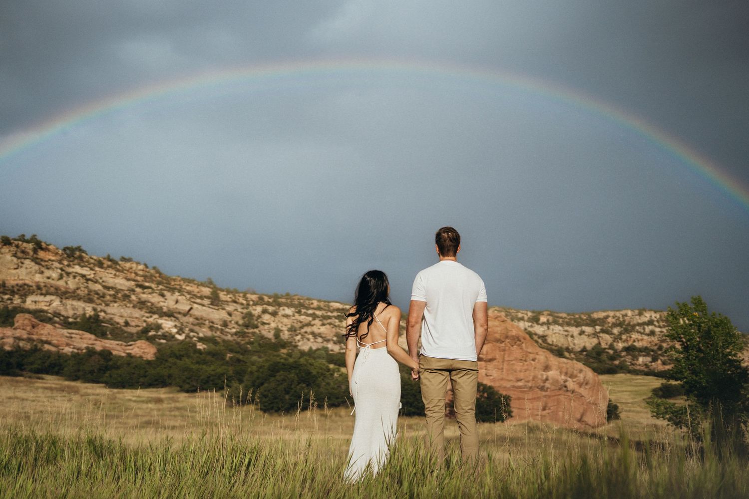 A rainbow arches over a scenic desert landscape with rocky cliffs and desert vegetation in the background.