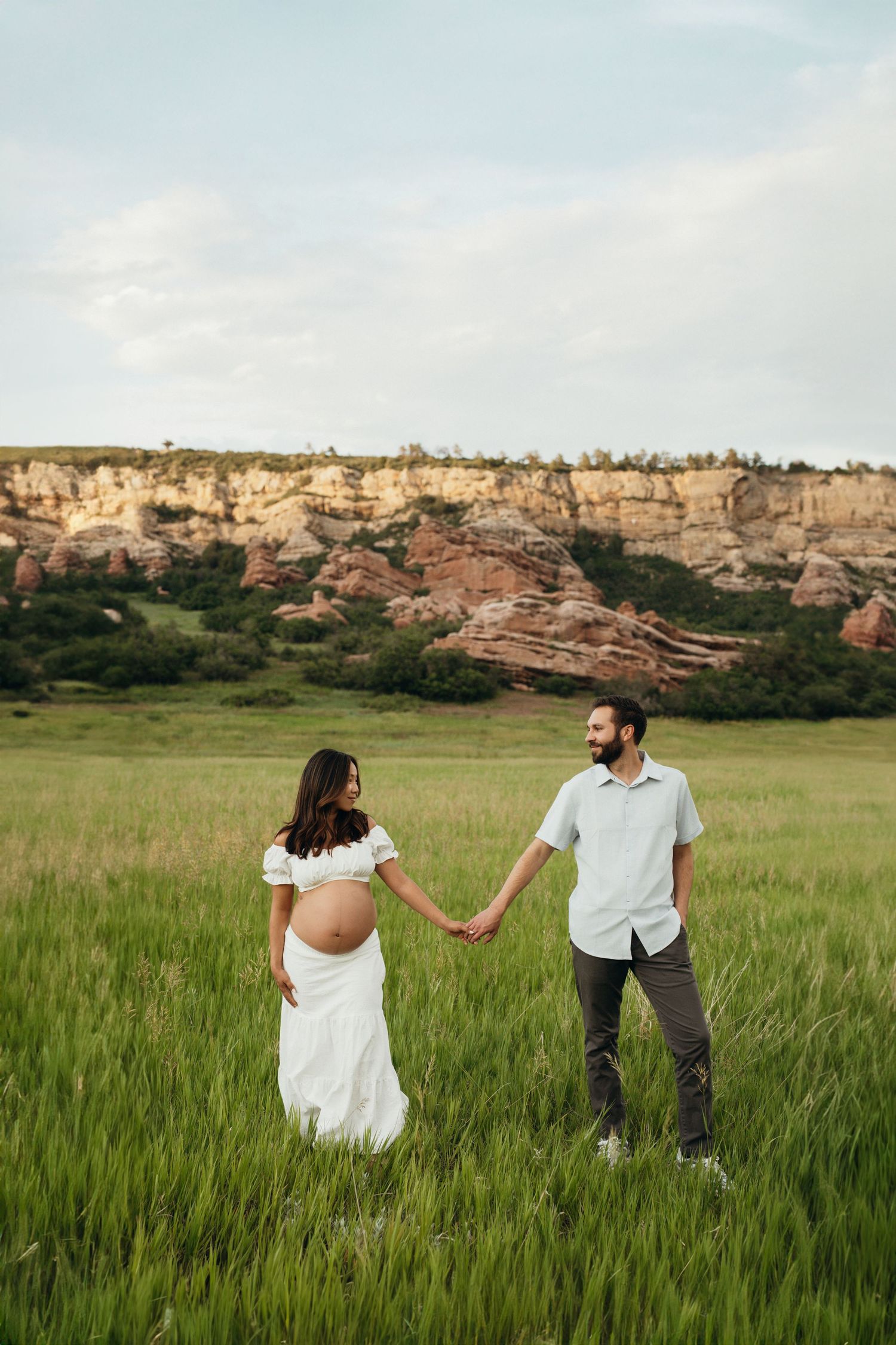 Couple walking through a lush green field with dramatic rock formations in the background.
