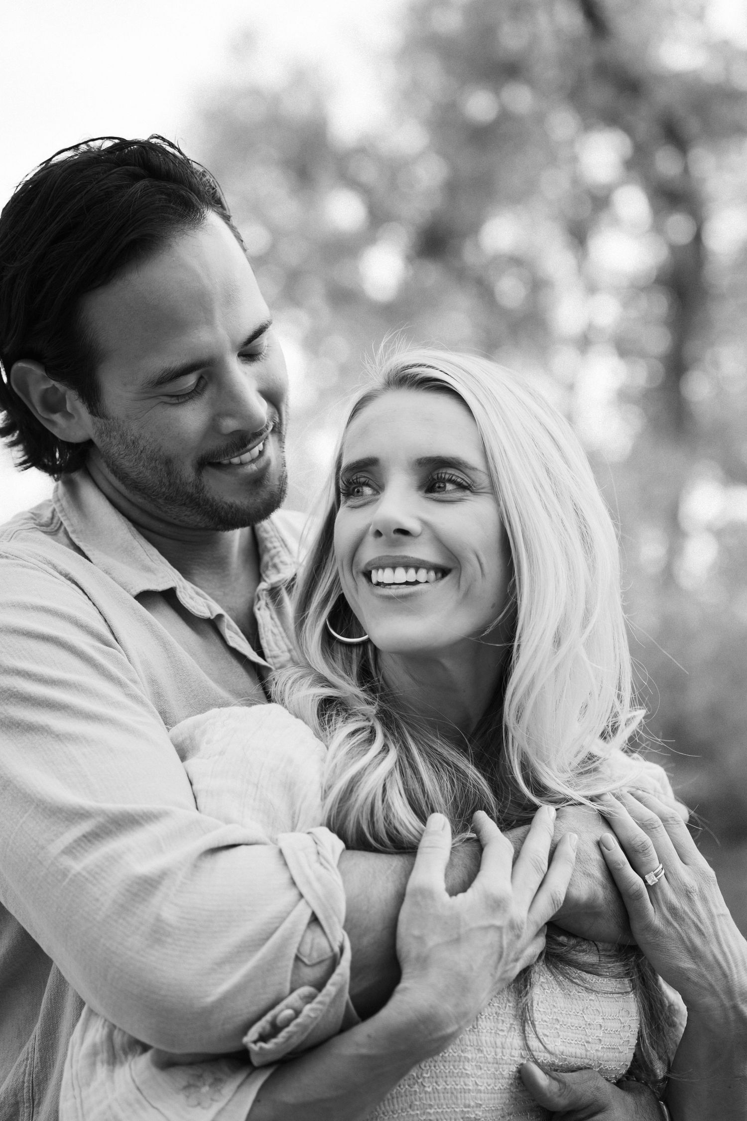 A black and white portrait of a couple sharing a loving embrace outdoors.
