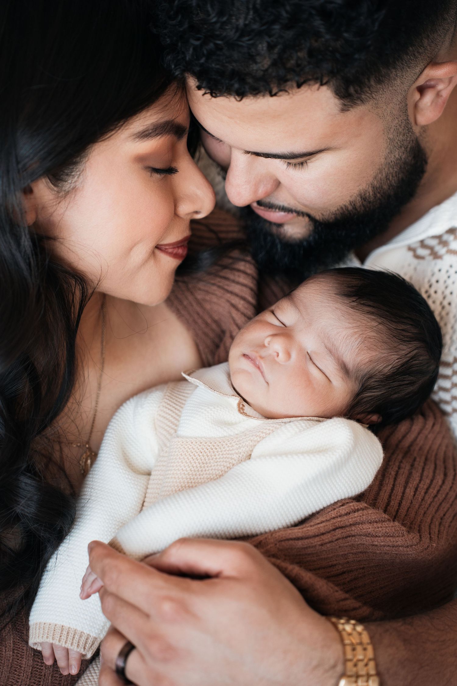 A tender family moment as parents share an intimate moment with their sleeping baby wearing a white sweater.