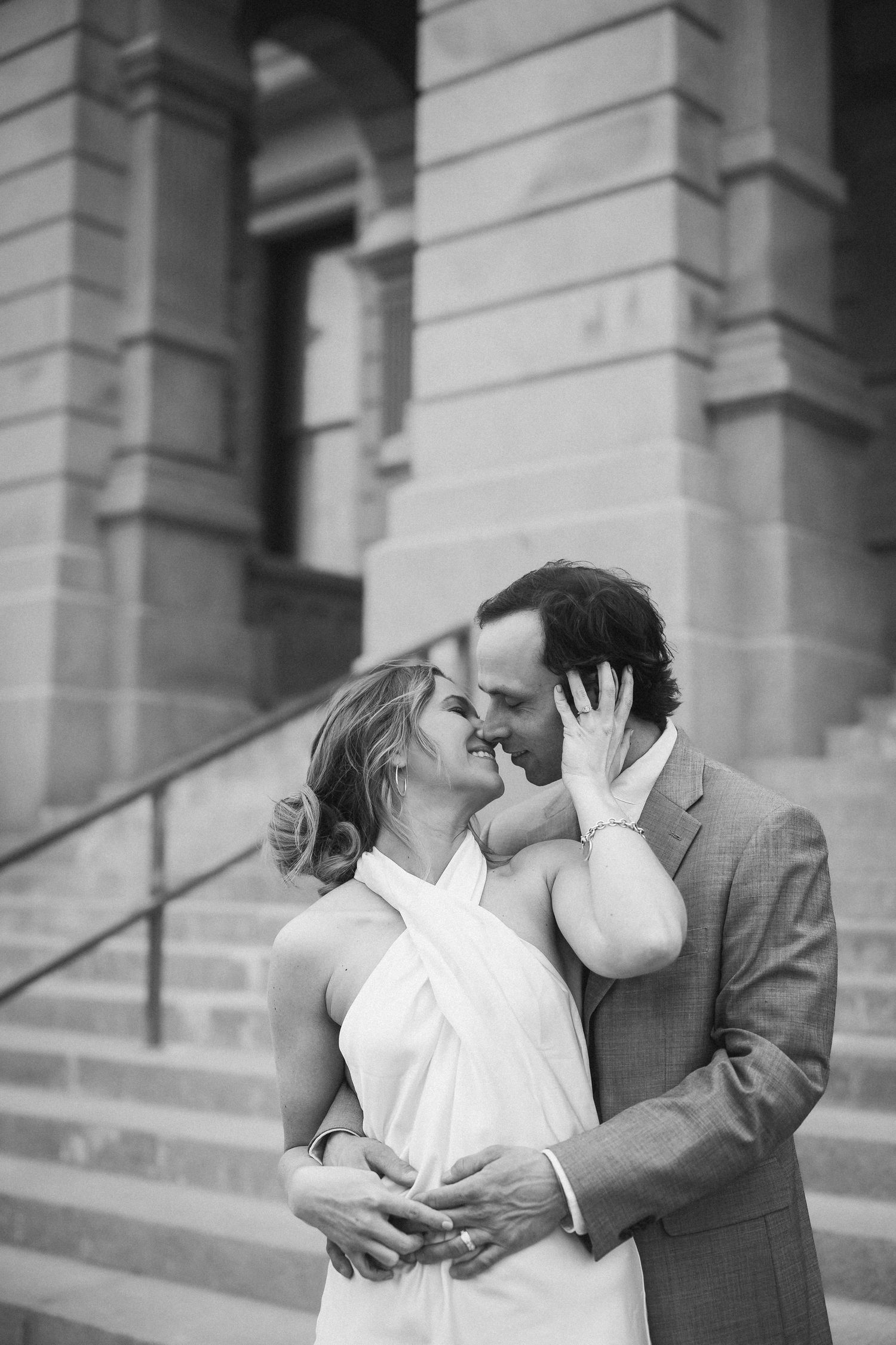 A romantic black and white wedding portrait of a couple embracing on grand stone steps of a historic building.