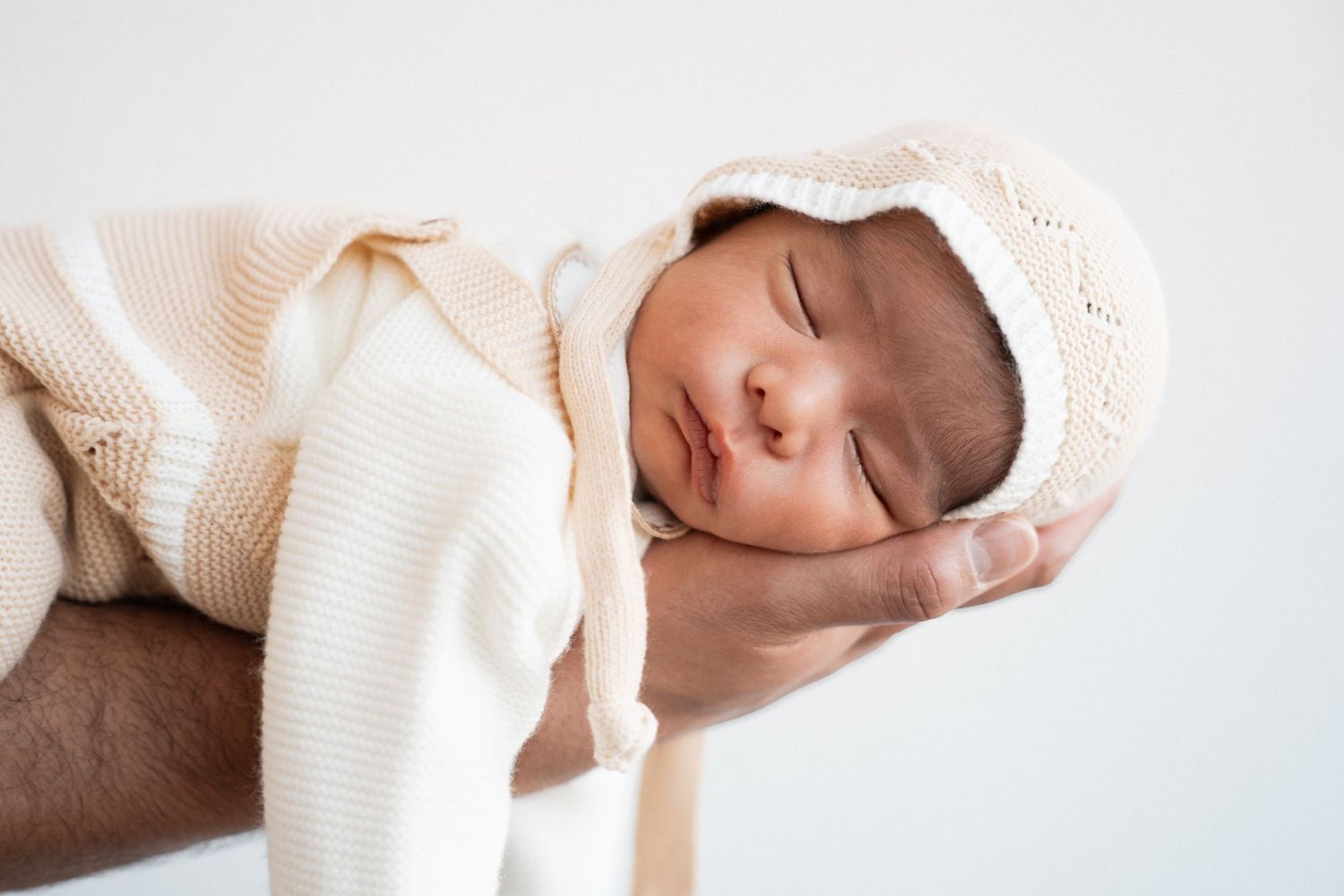 Peaceful newborn baby wrapped in soft cream knit blanket and bonnet sleeping sweetly.