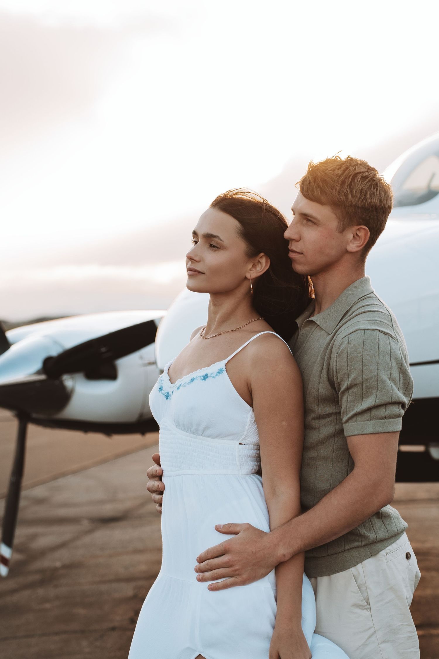 Romantic couple embraces near a small aircraft during sunset at an airfield.