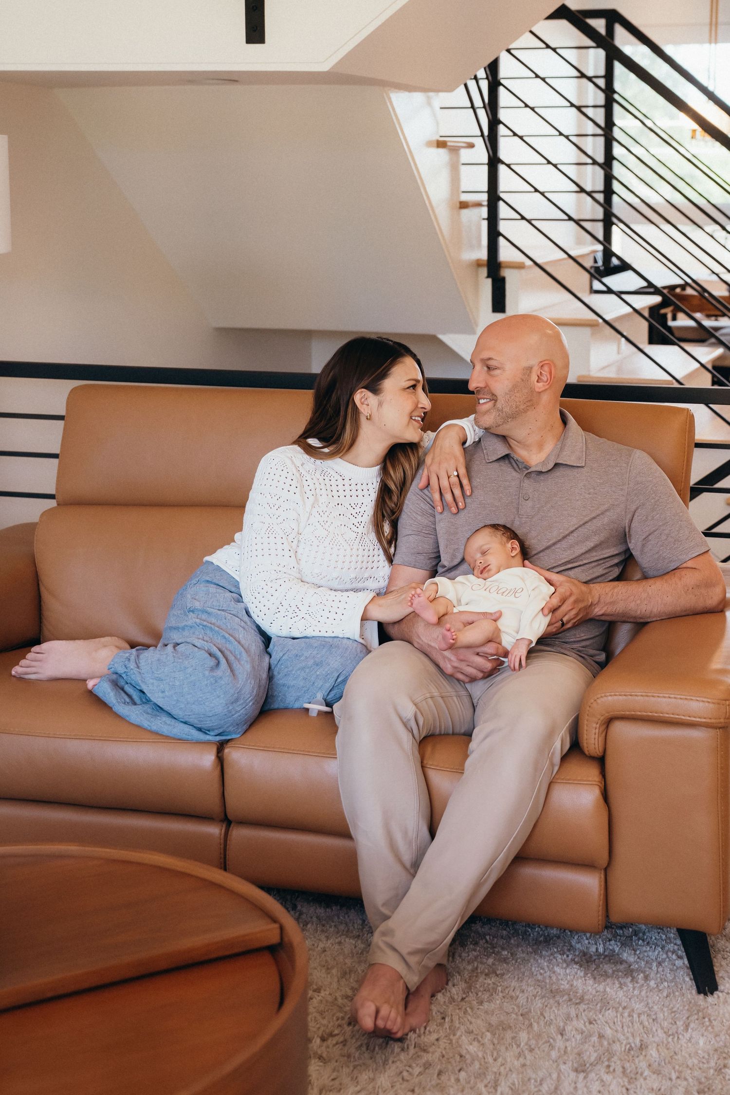 A family relaxes together on a brown leather sectional sofa in a modern living room.