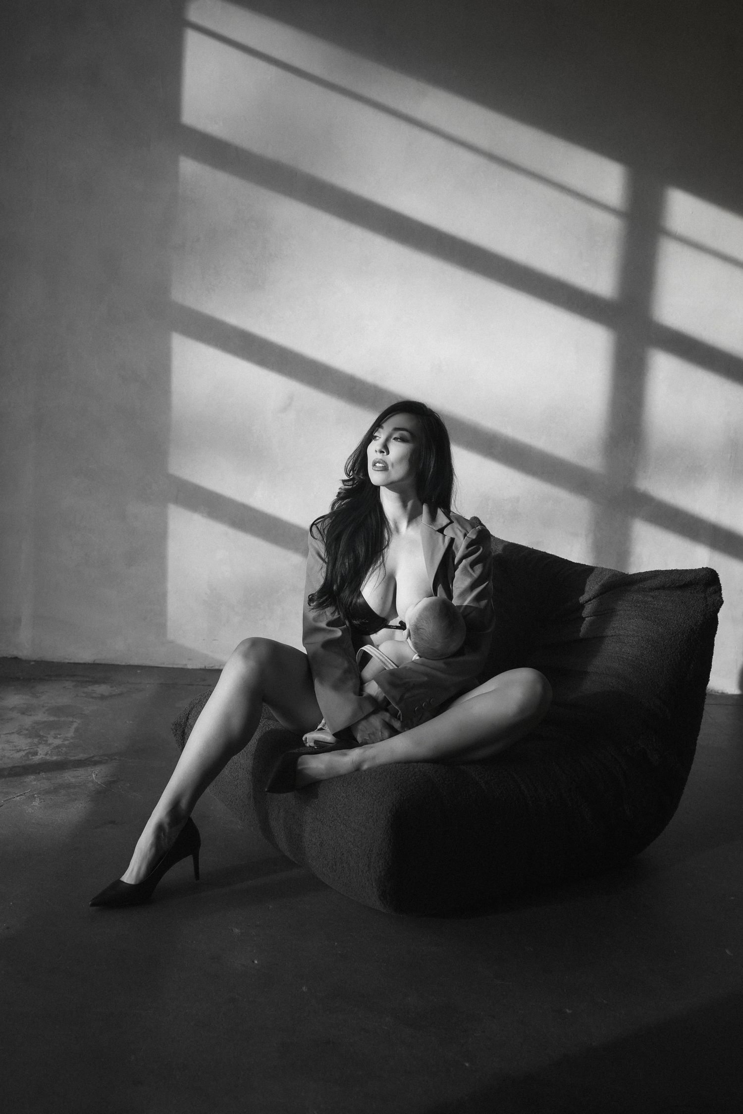 Dramatic black and white portrait of someone reclining on dark couch with geometric window light patterns on wall.