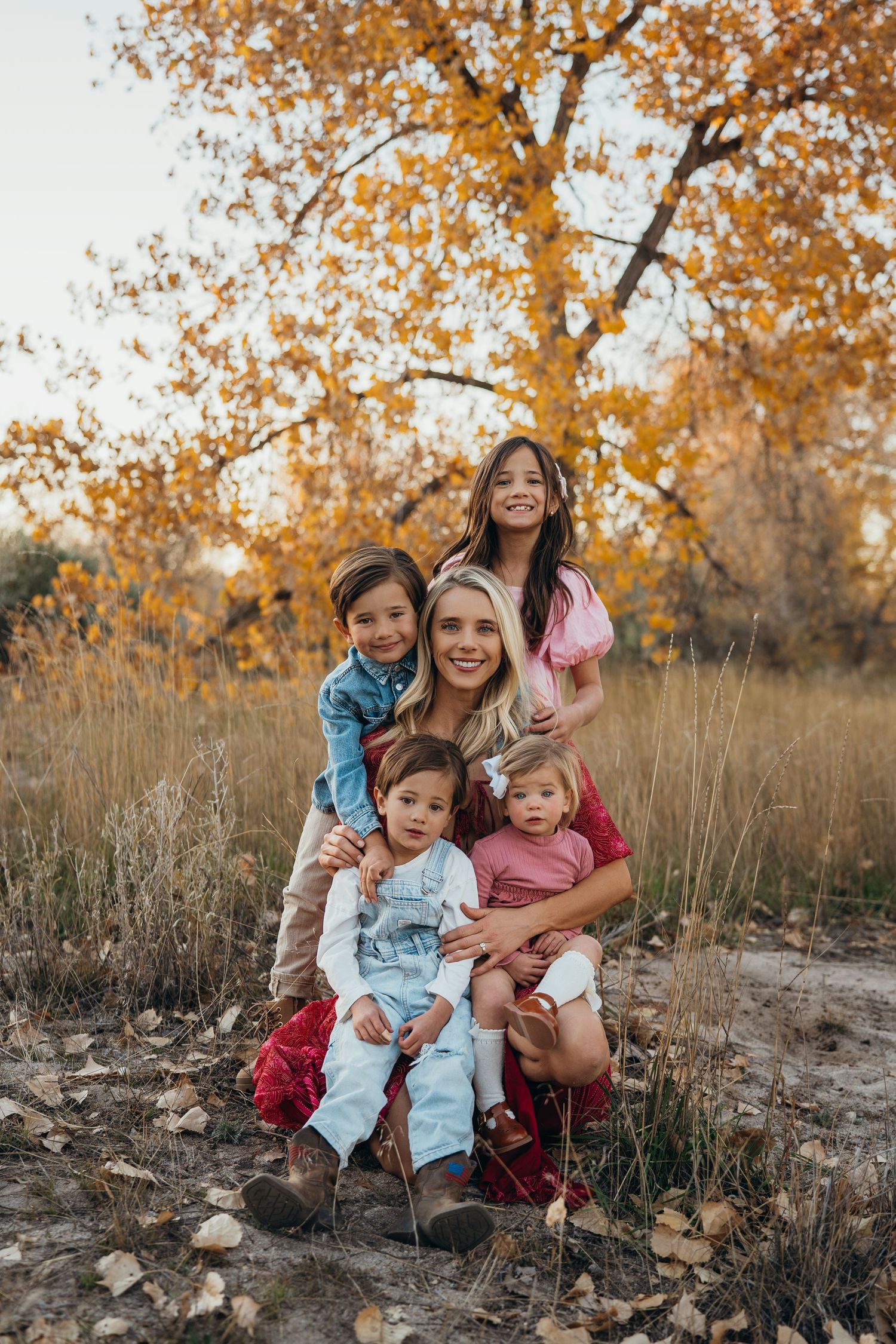 A family sits together on rocky ground surrounded by autumn trees with golden leaves in the background.