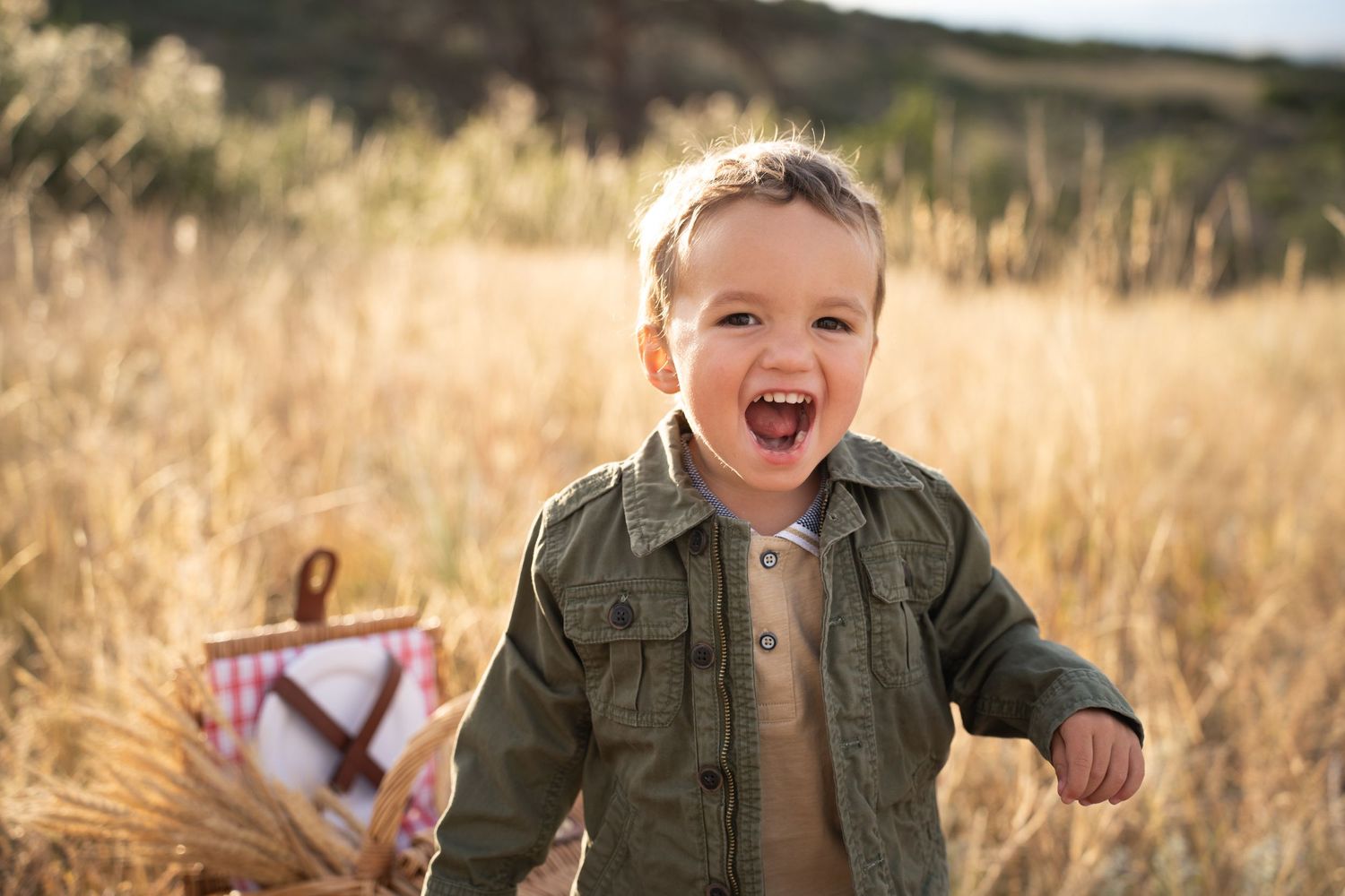 Joyful child laughing outdoors in a field wearing an olive green jacket.