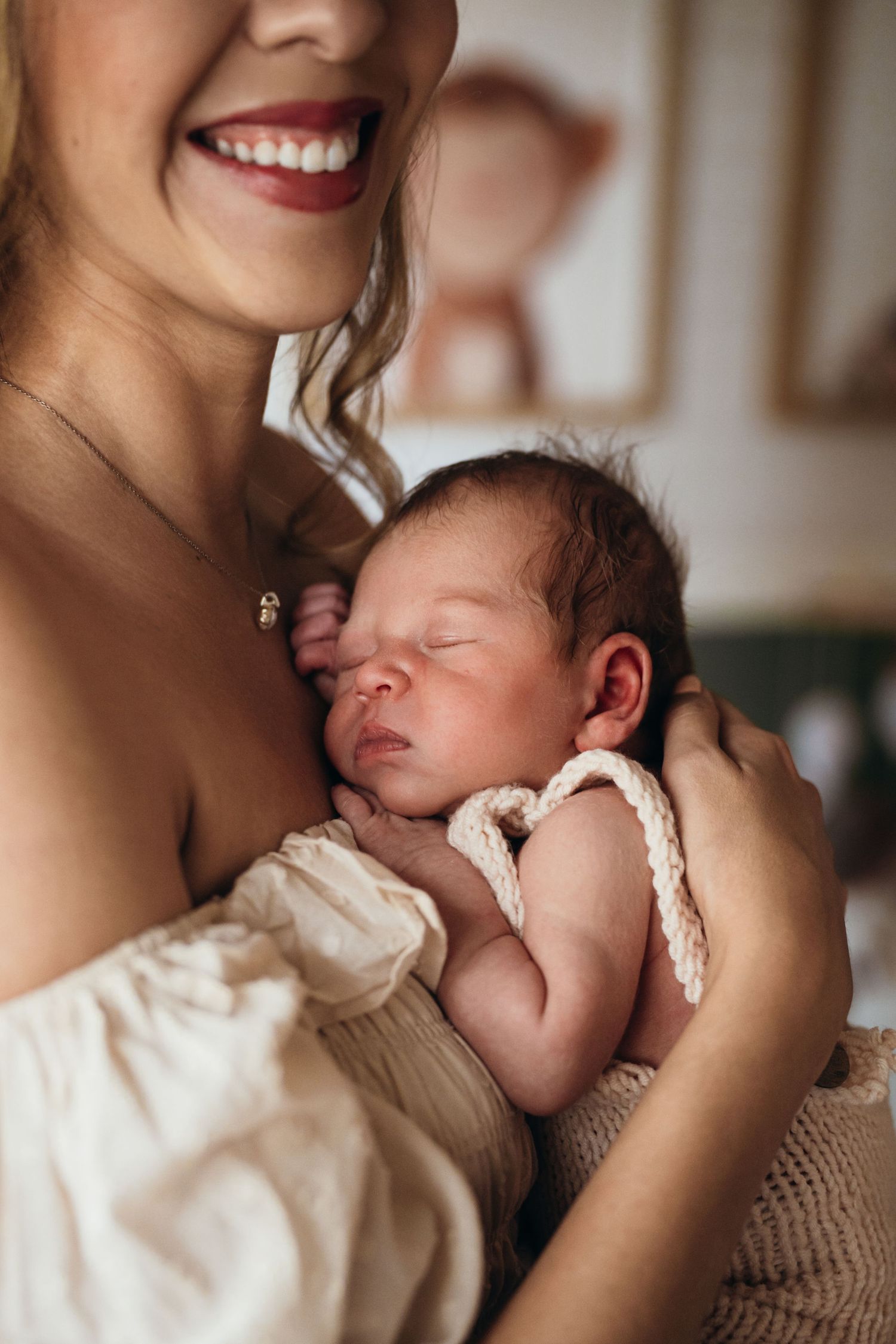 A tender moment as a sleeping newborn baby rests snuggled up in white fabric against their mother's chest.