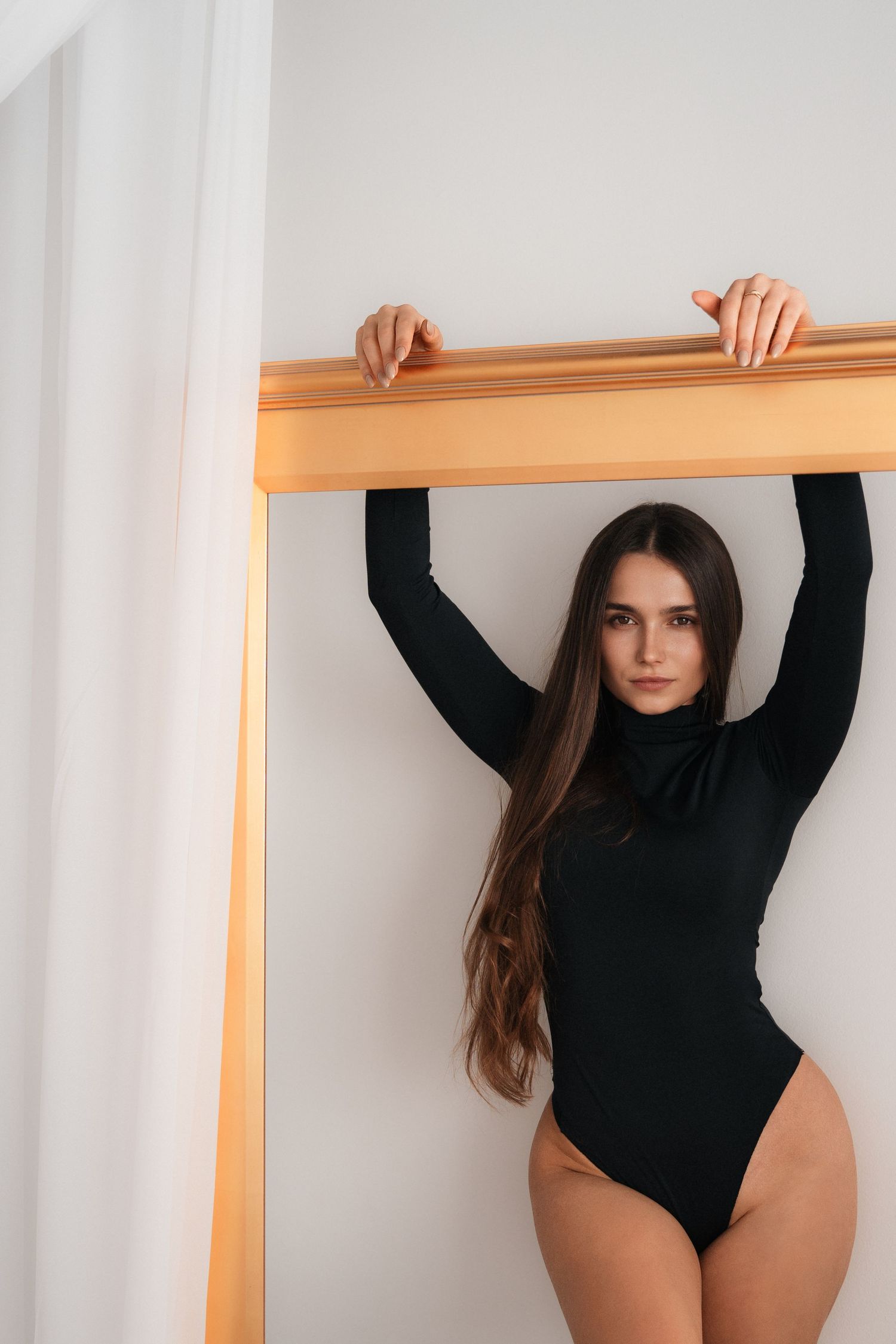 Athletic pose in black bodysuit against white doorframe.
