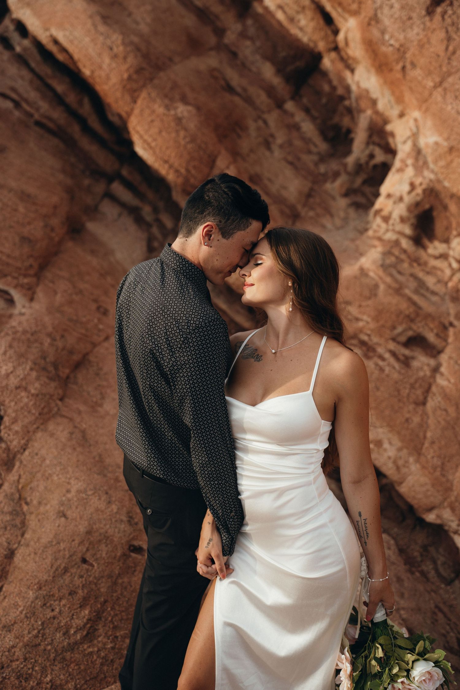 Romantic couple embraces against stunning red rock formations in a desert setting.