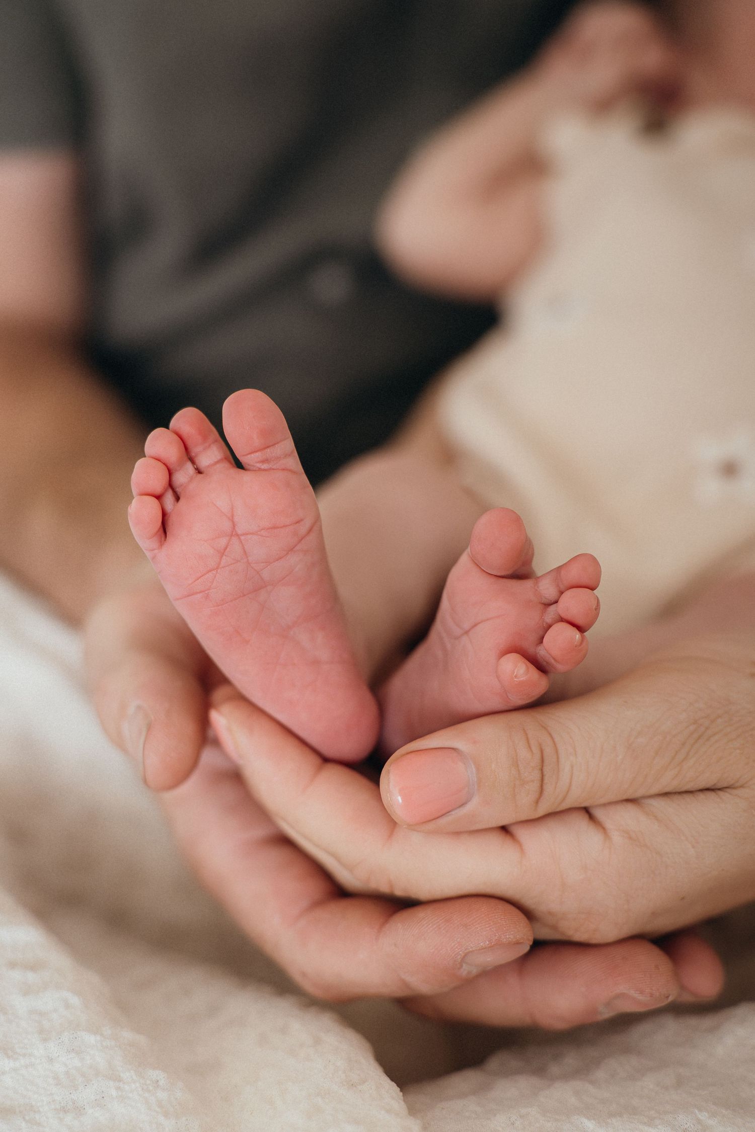 Close-up sequence of tiny baby feet being gently held in adult hands against a soft cream-colored background.