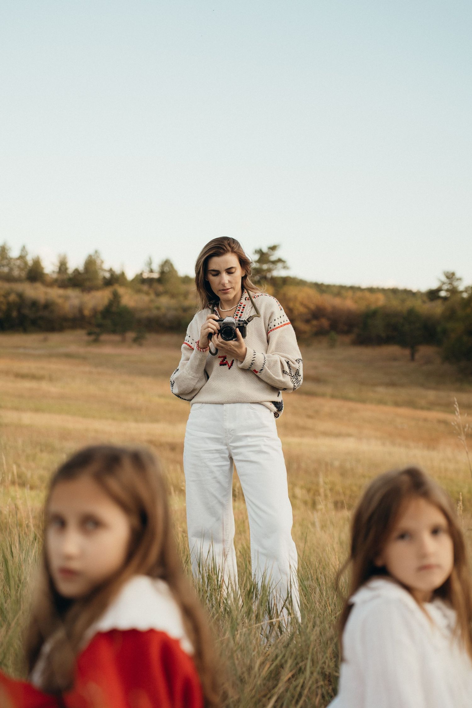 A photographer takes pictures in a golden field at sunset while two children sit in the foreground.