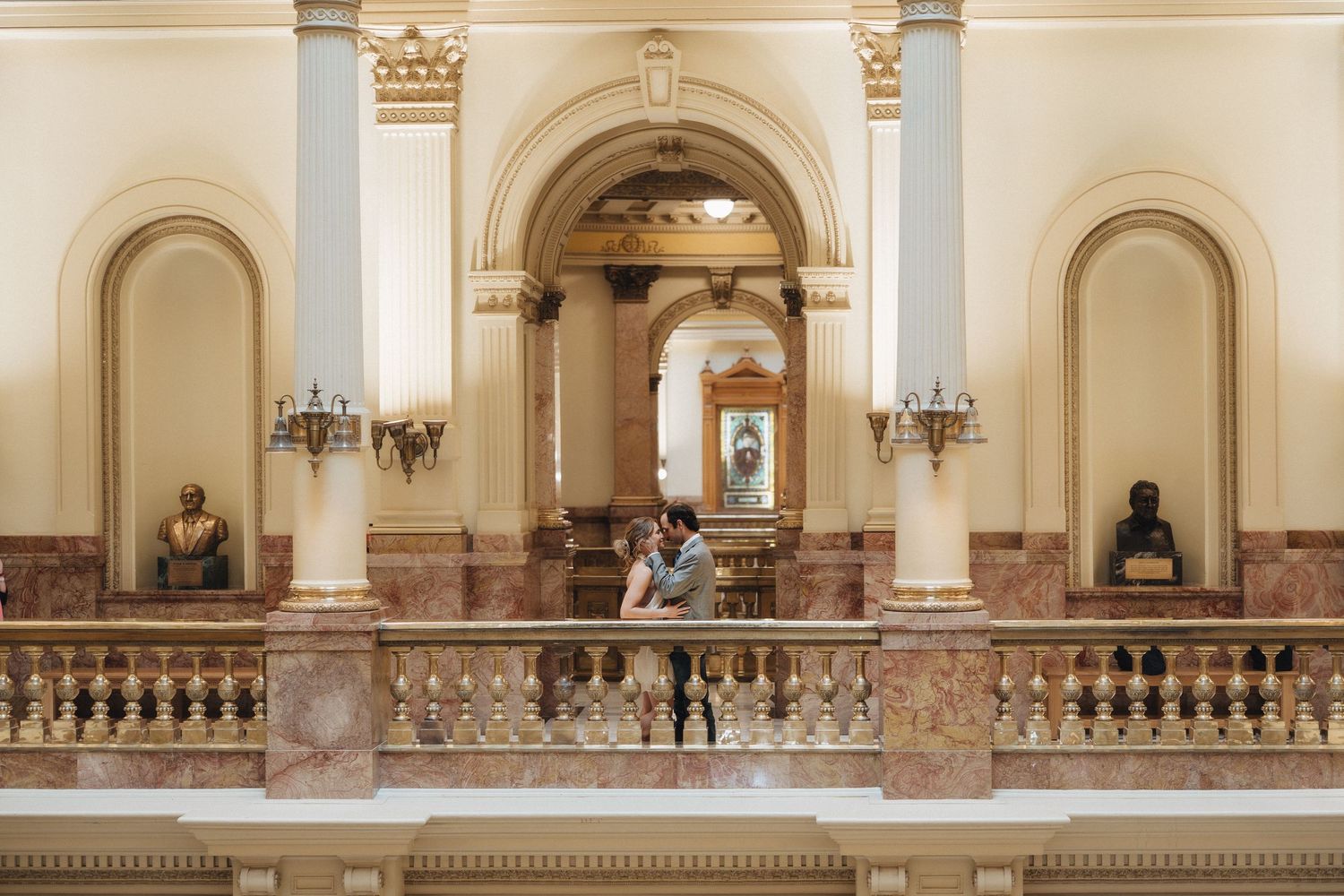 Elegant marble balustrade and columns in a grand historic building interior with ornate wall sconces and architectural details.