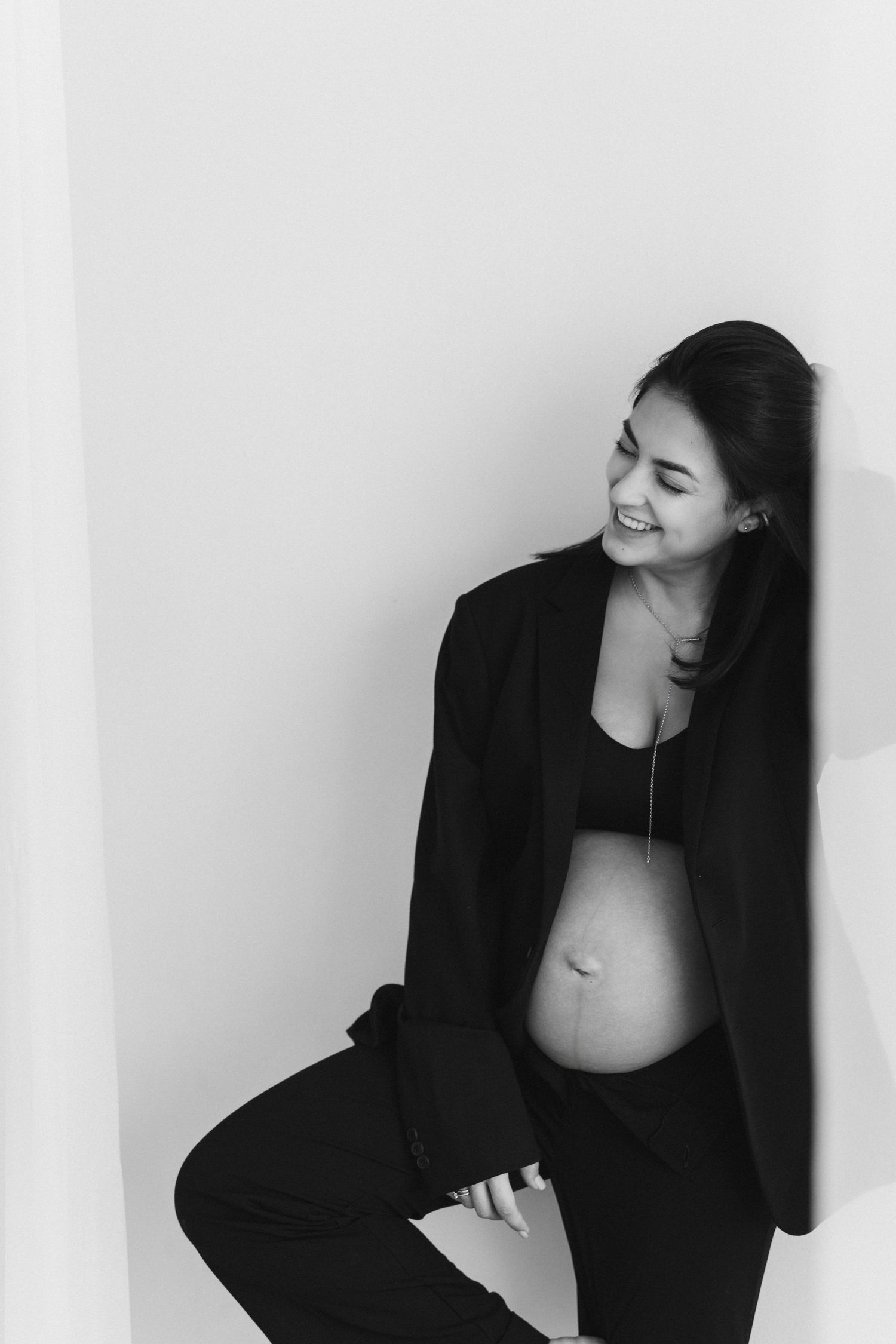 Black and white artistic maternity photo showing woman in blazer against minimal background.