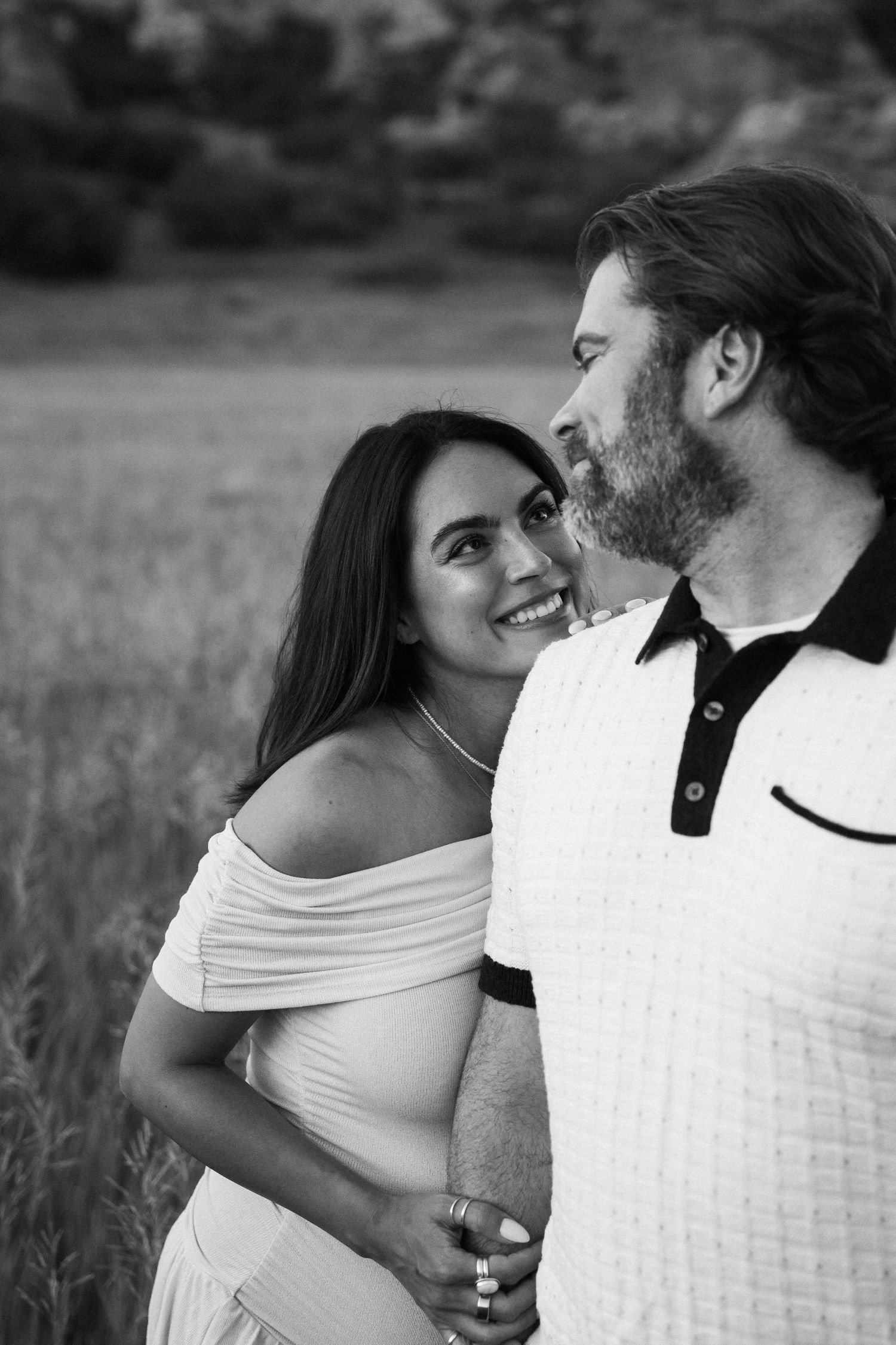 A loving couple shares an intimate moment together in a field, captured in black and white photography.