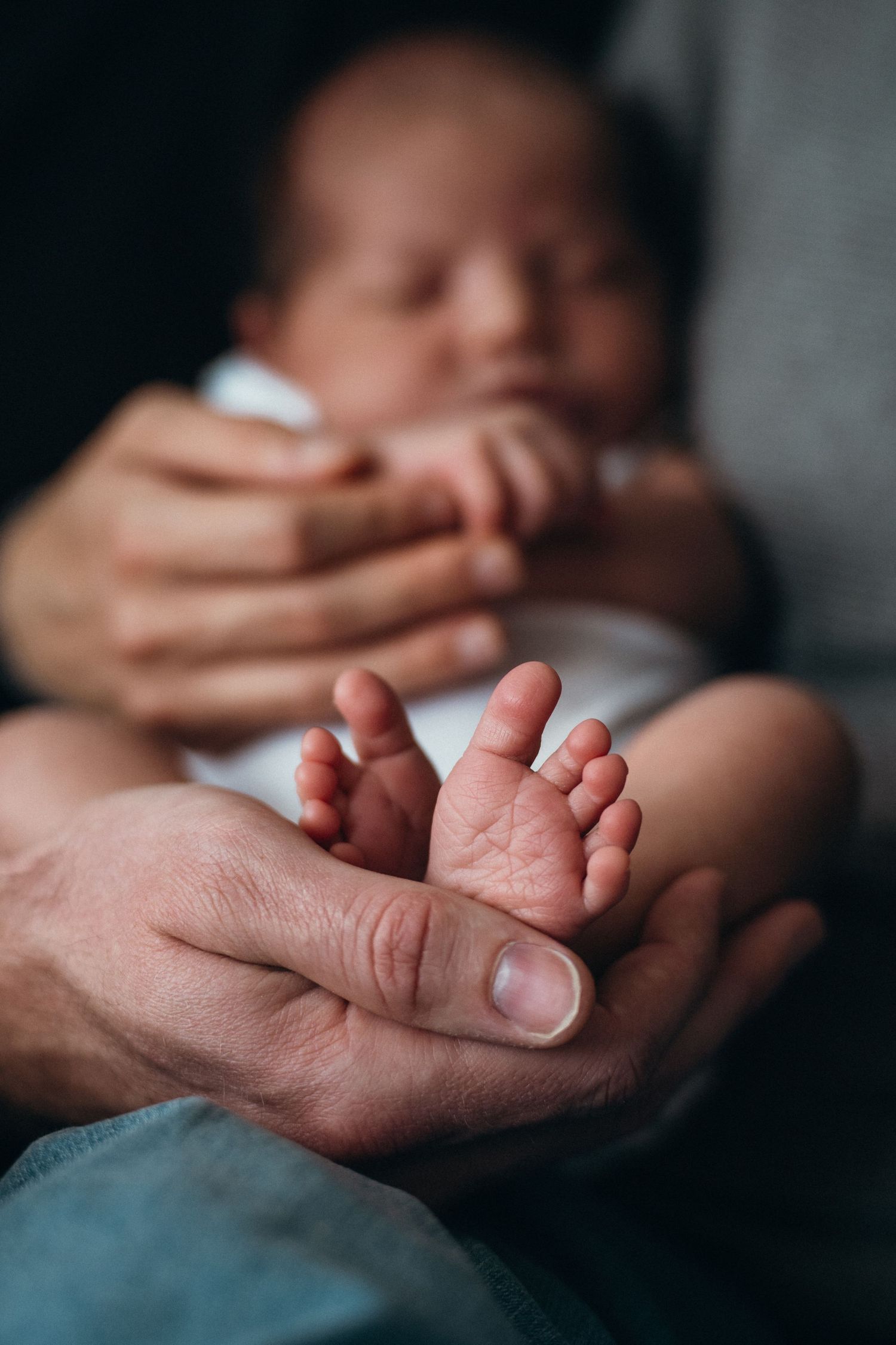 Close-up of tiny baby feet being gently cradled in adult hands while infant rests in soft focus background.