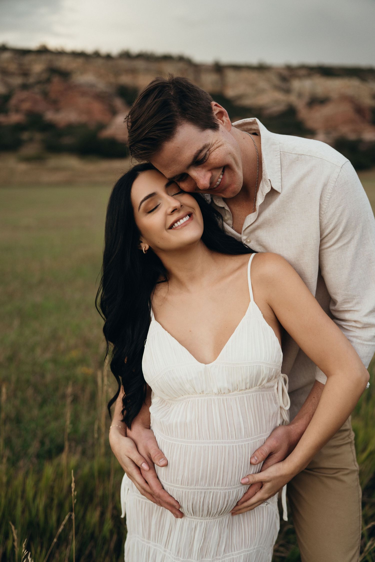 Romantic couple embraces in a field at sunset wearing coordinating white and beige outfits.