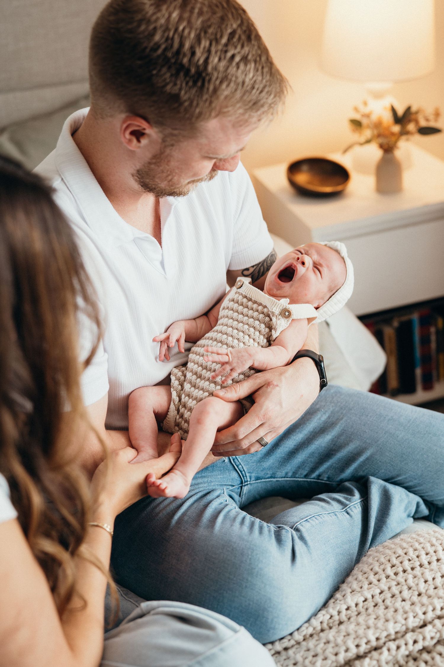 A yawning newborn baby wrapped in a striped blanket is cradled while being held in a cozy indoor setting.