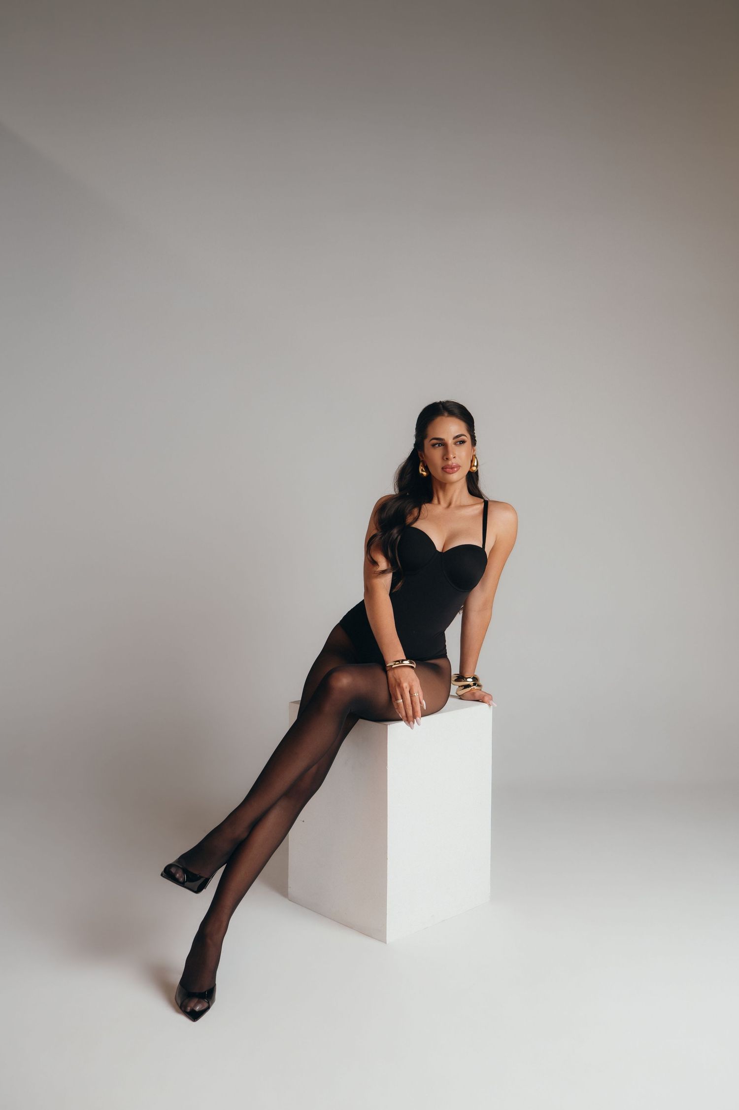 Fashion model in black bodysuit and sheer stockings poses elegantly against white backdrop in artistic photo series.
