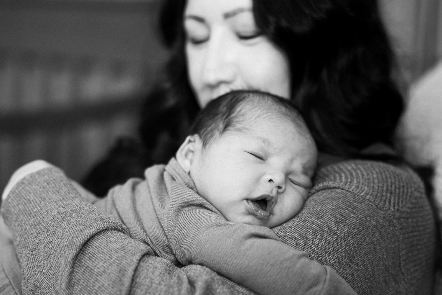 A sleeping baby rests peacefully on a caregiver's shoulder in a tender black and white portrait.