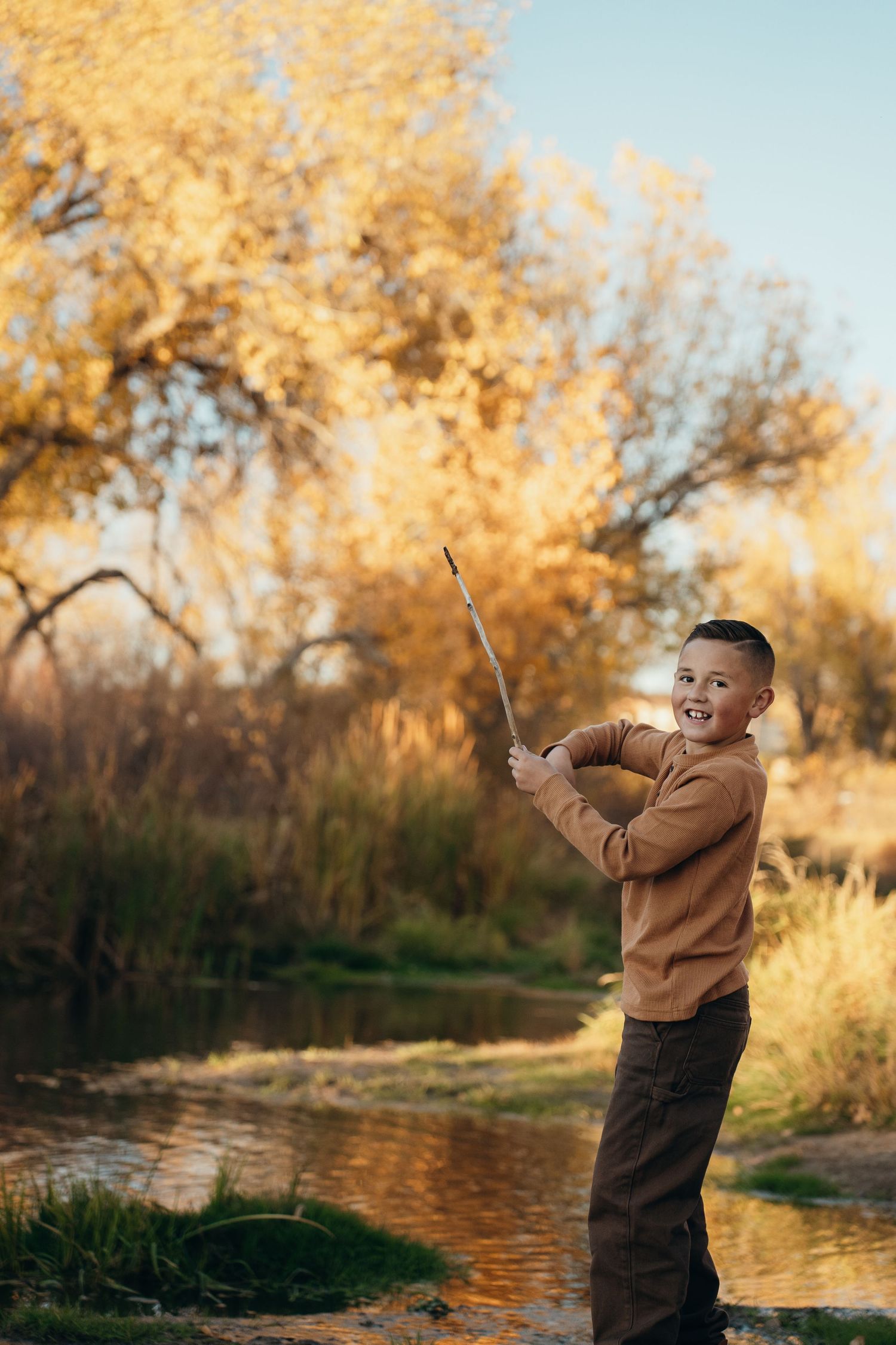 Person in brown jacket stands by autumn pond during golden hour while fishing with a rod and reel.