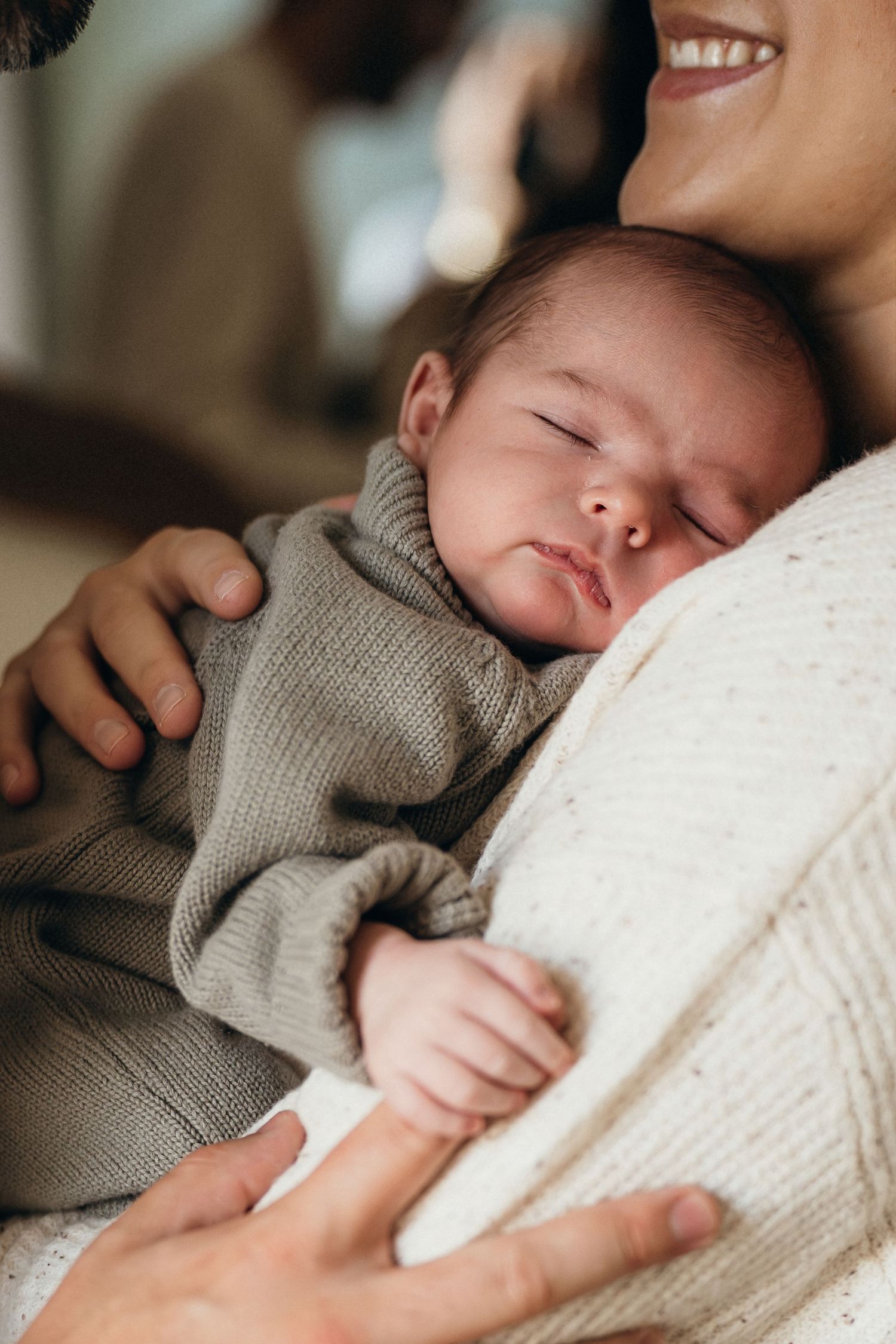 Peaceful sleeping baby in gray sweater rests against parent in tender moment at home.
