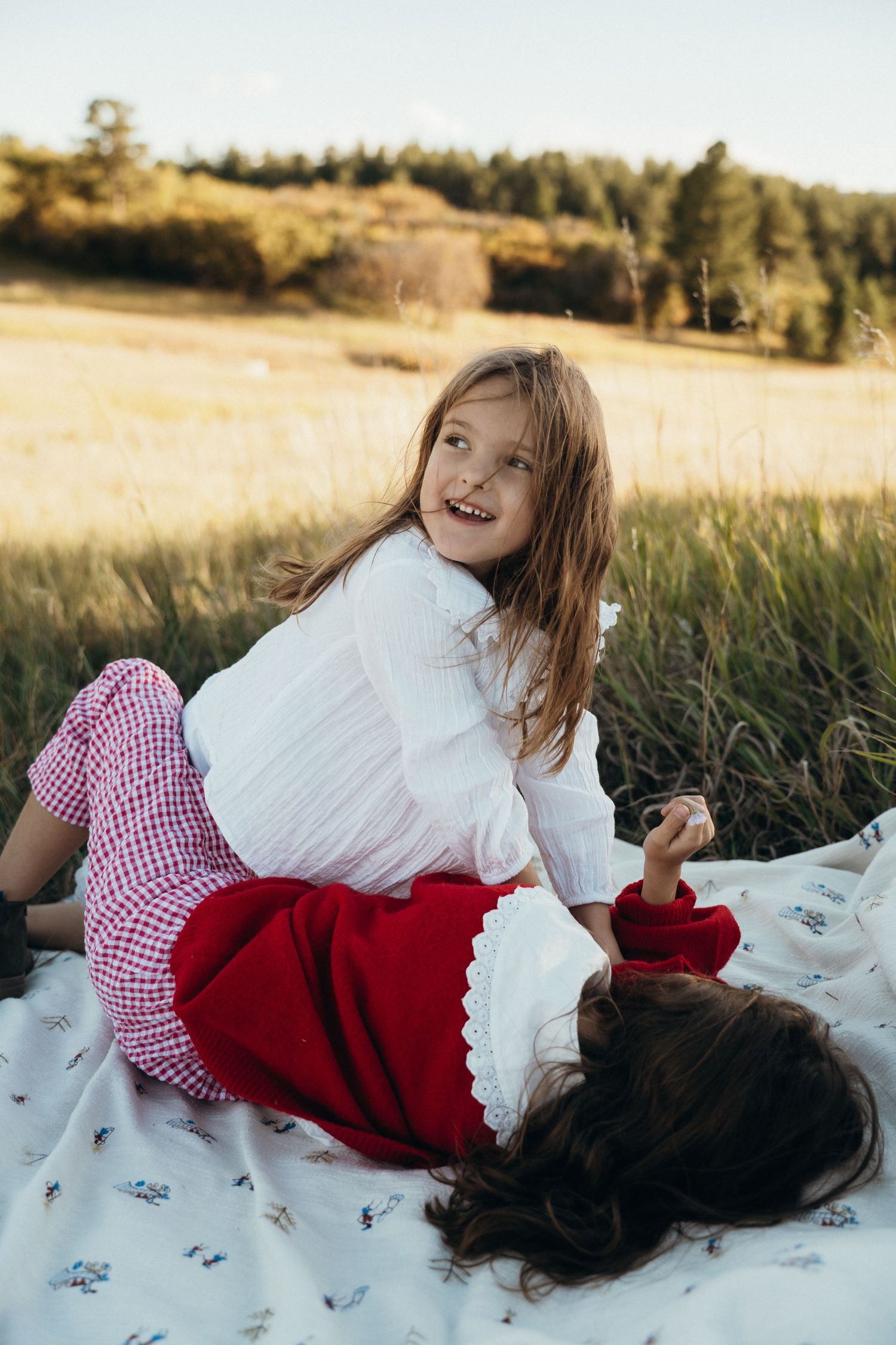 Children laughing and playing together on a white blanket in a sunny field at golden hour.