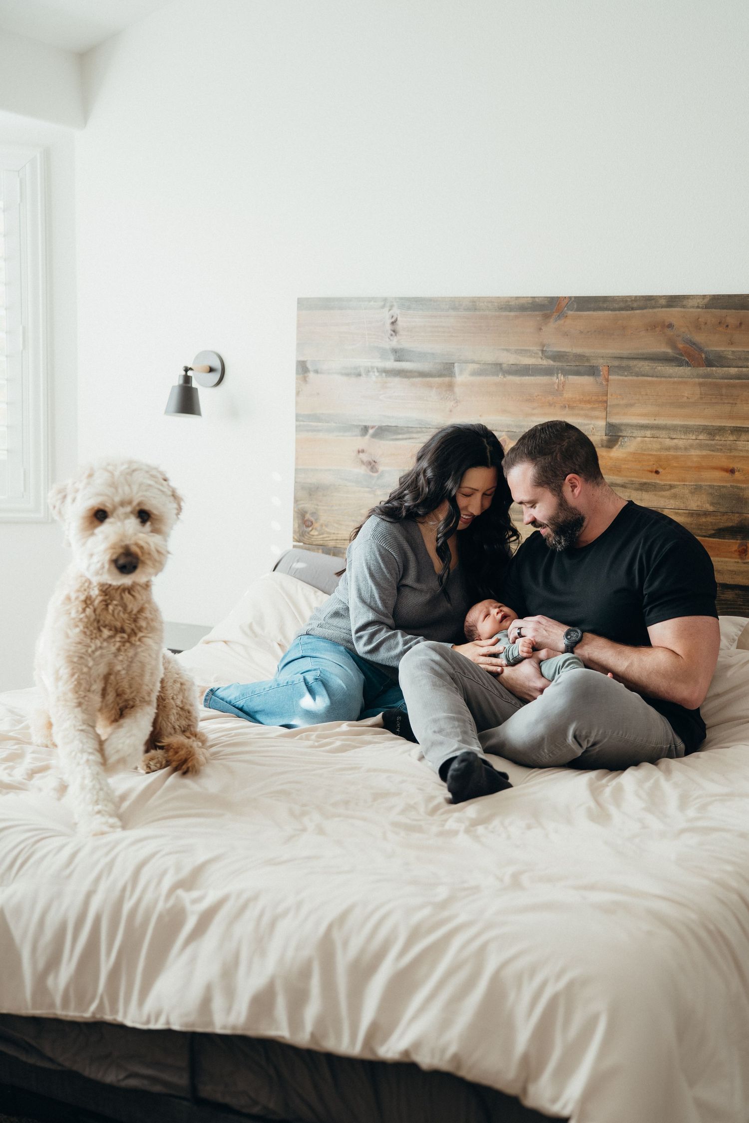 A couple lounges on a white bed with their fluffy white dog, creating a cozy and intimate lifestyle scene.