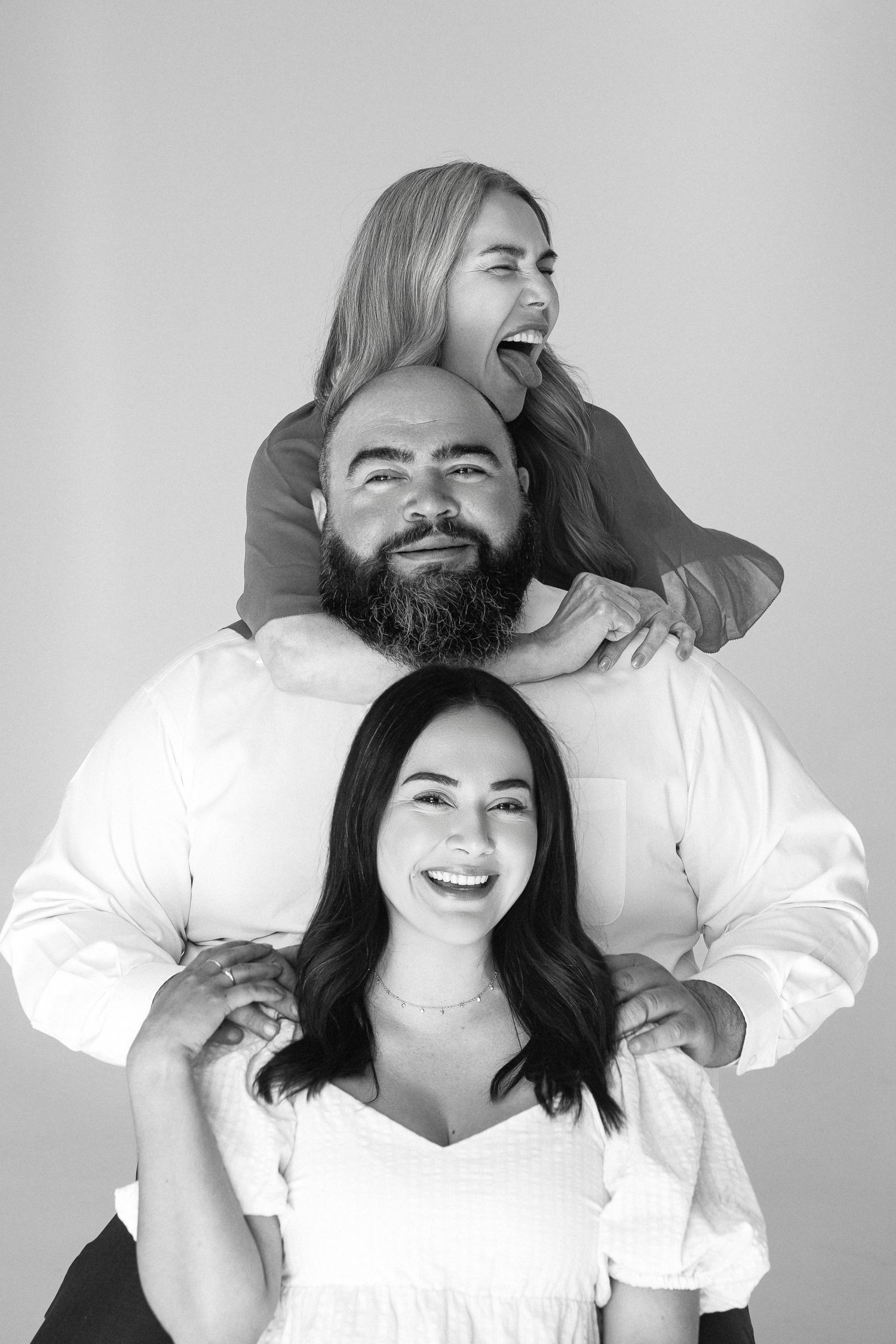 A black and white portrait of three people joyfully smiling and laughing together in a playful posed composition.