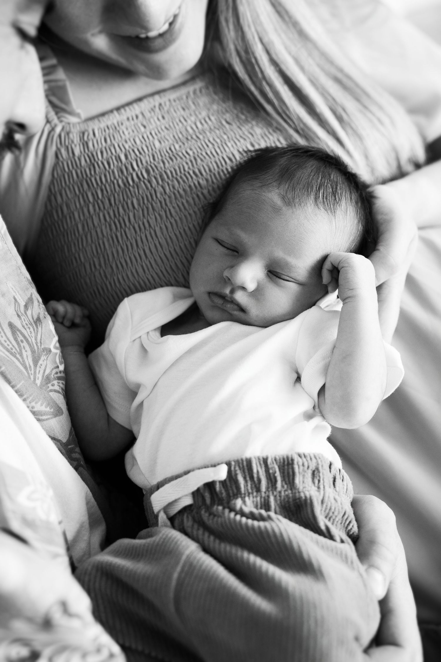 A series of four black and white photos showing a peaceful sleeping newborn baby swaddled in white blankets.