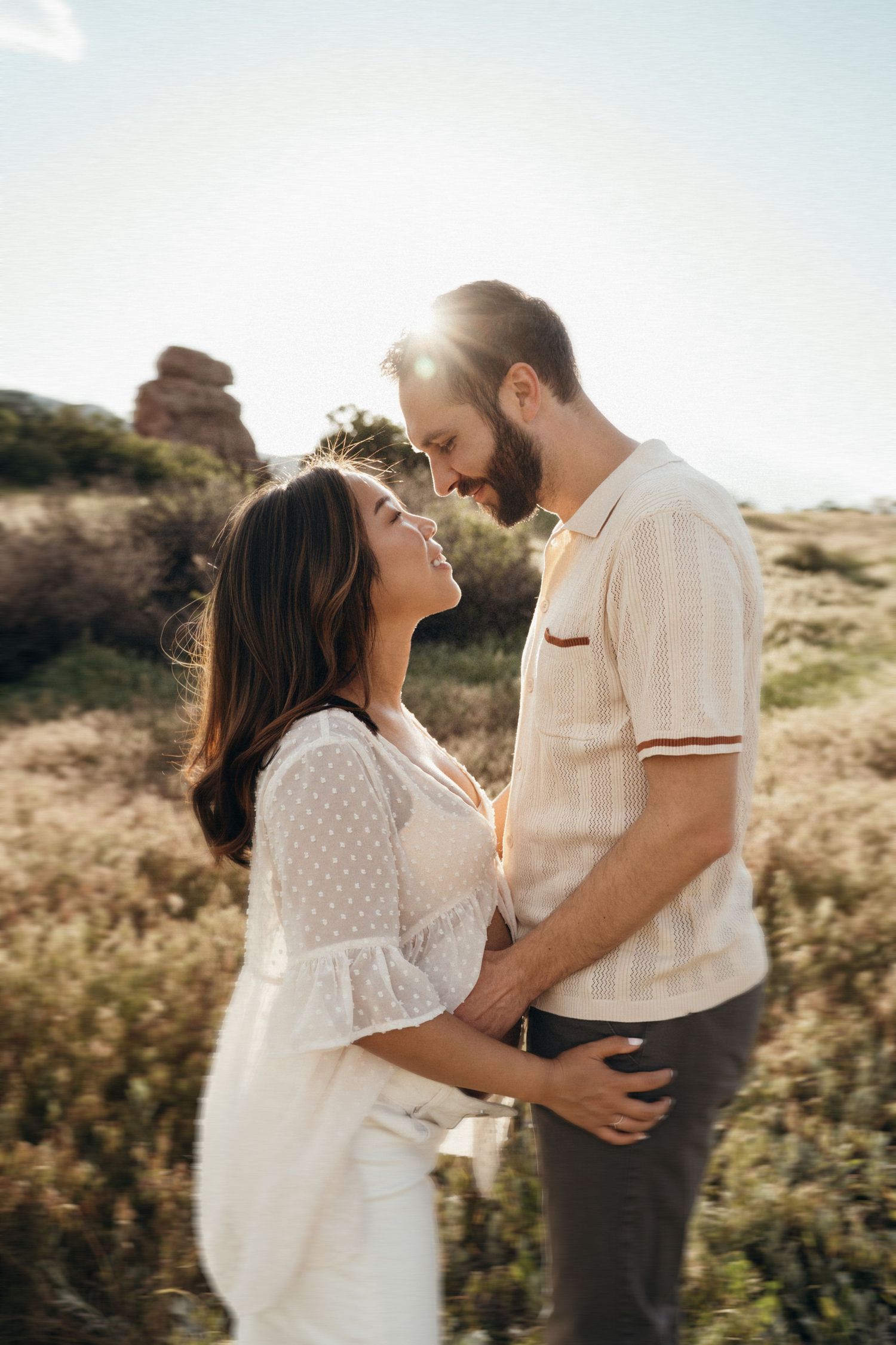 A couple shares intimate moments during a golden hour photoshoot in a desert landscape with mountain views.