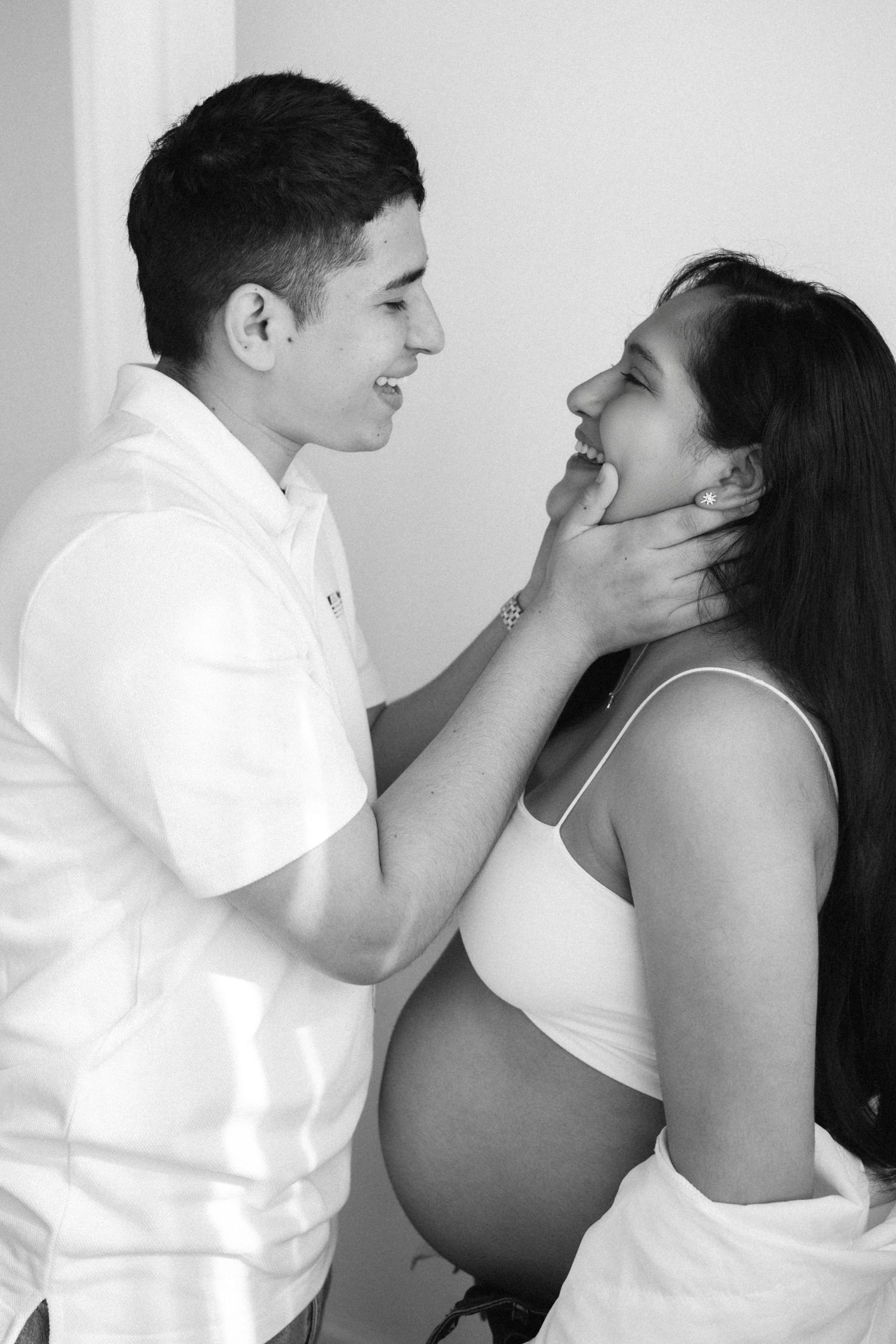 A black and white maternity photo shows an intimate moment between a couple in white clothing.