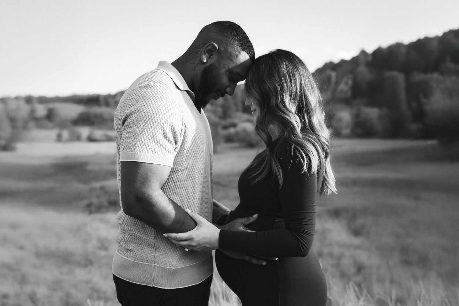Black and white outdoor maternity photo of couple embracing in field.