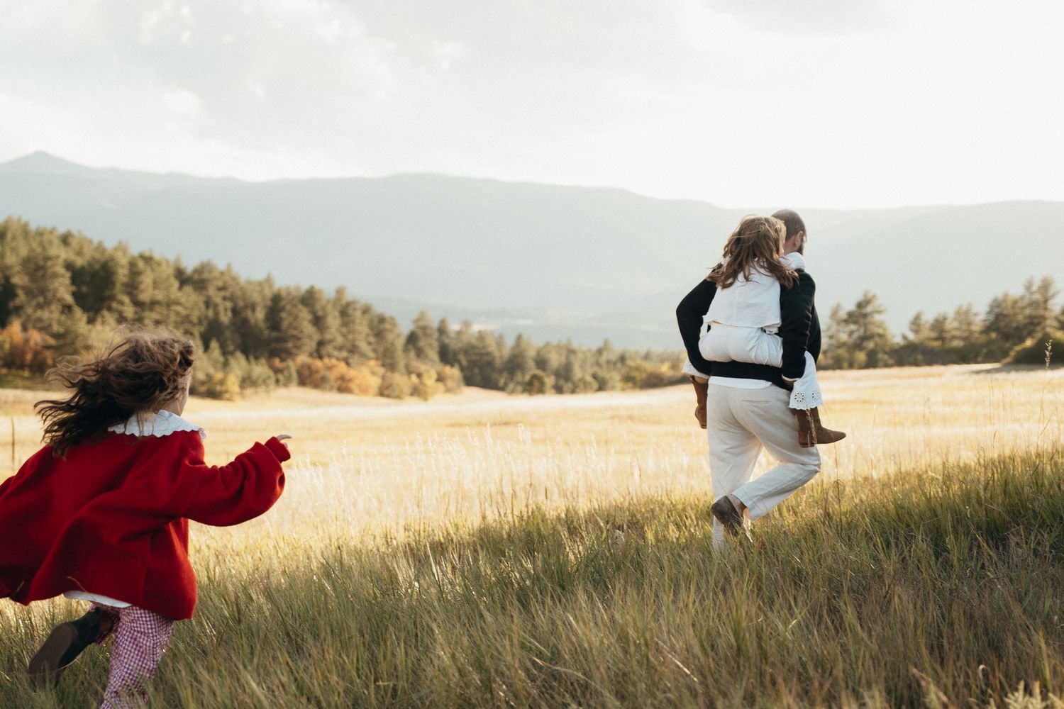 A series of silhouettes walking through a golden field at sunset with mountains in the background.