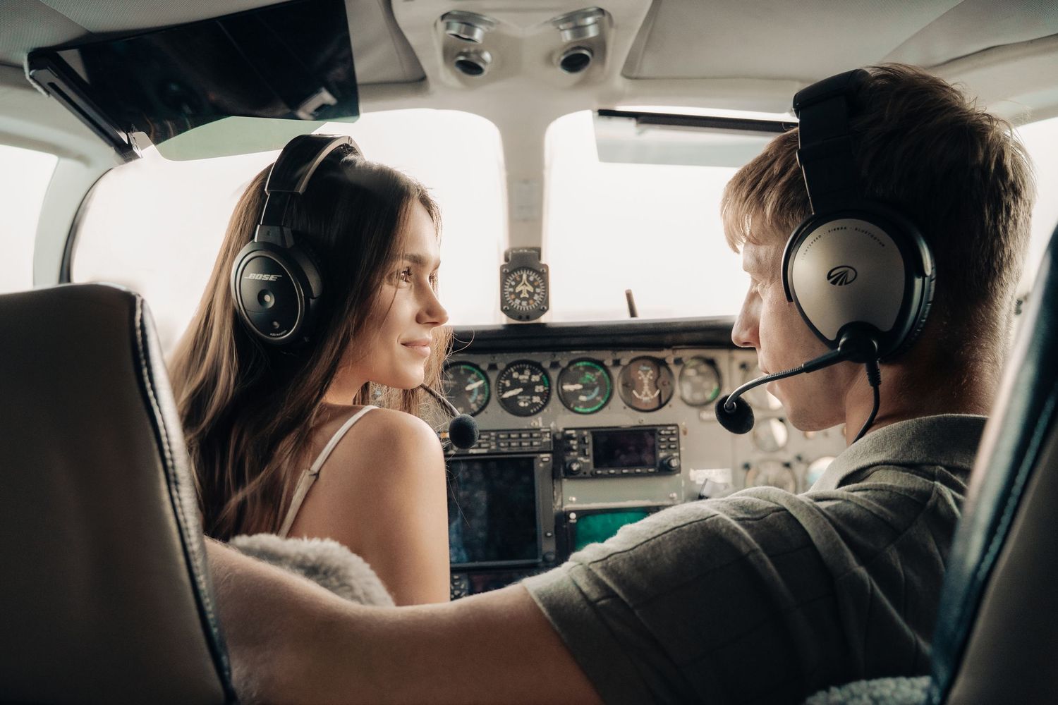 Two passengers wearing headsets sit in the cockpit of a small private aircraft during flight.