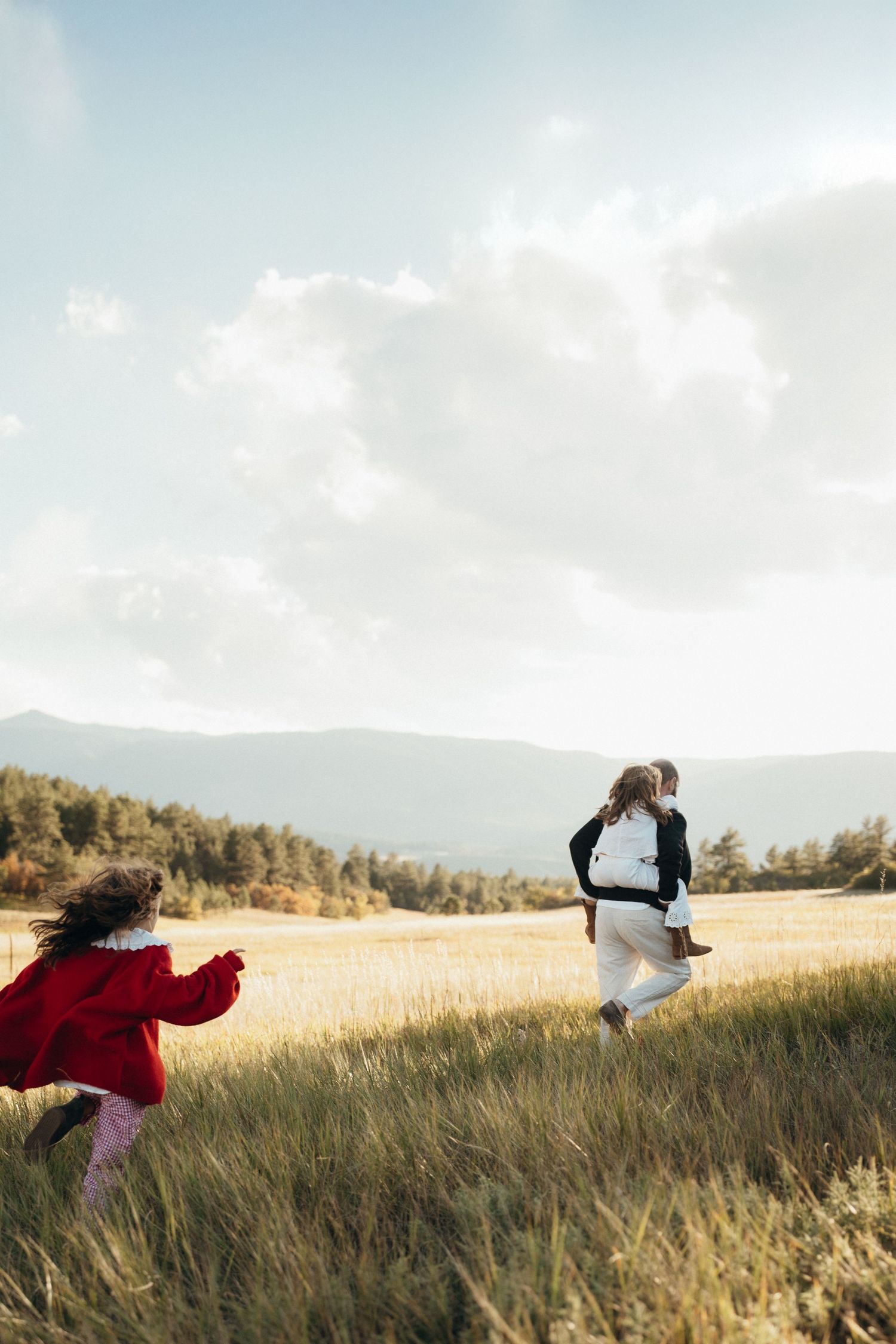 A sequence of people running through a golden grass field at sunset with mountains in the background.