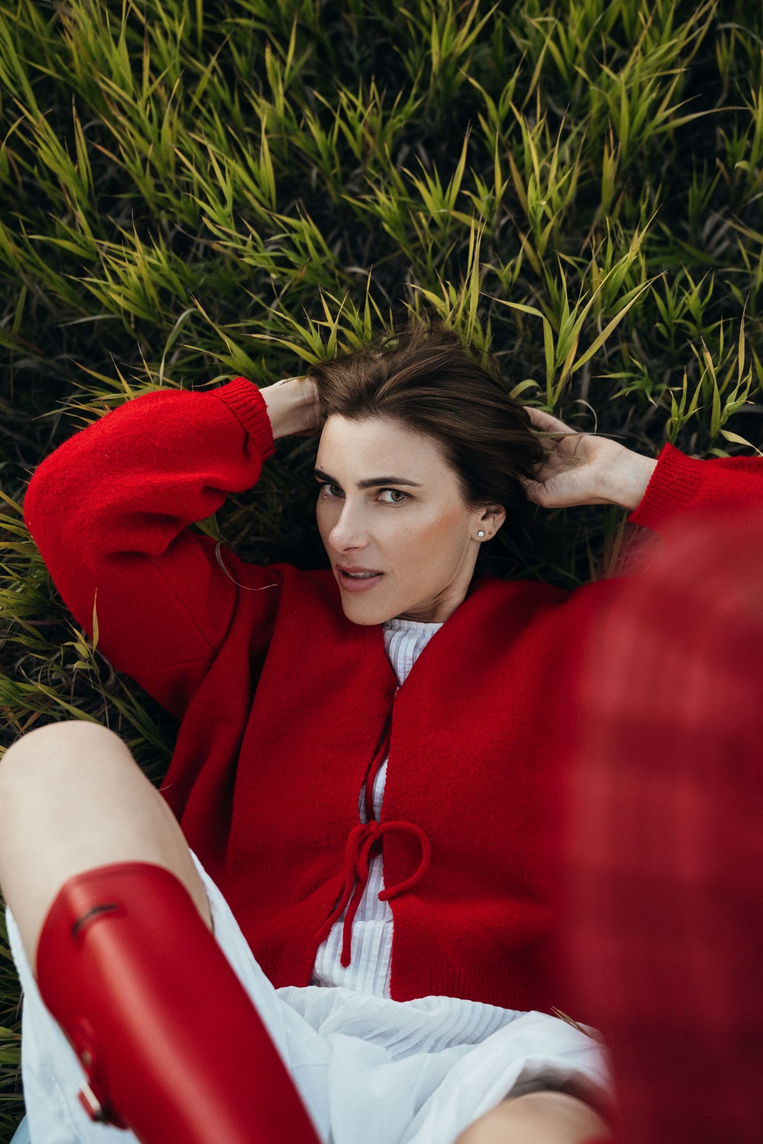 A person in a bright red sweater lies in green grass wearing white clothing and a relaxed pose.